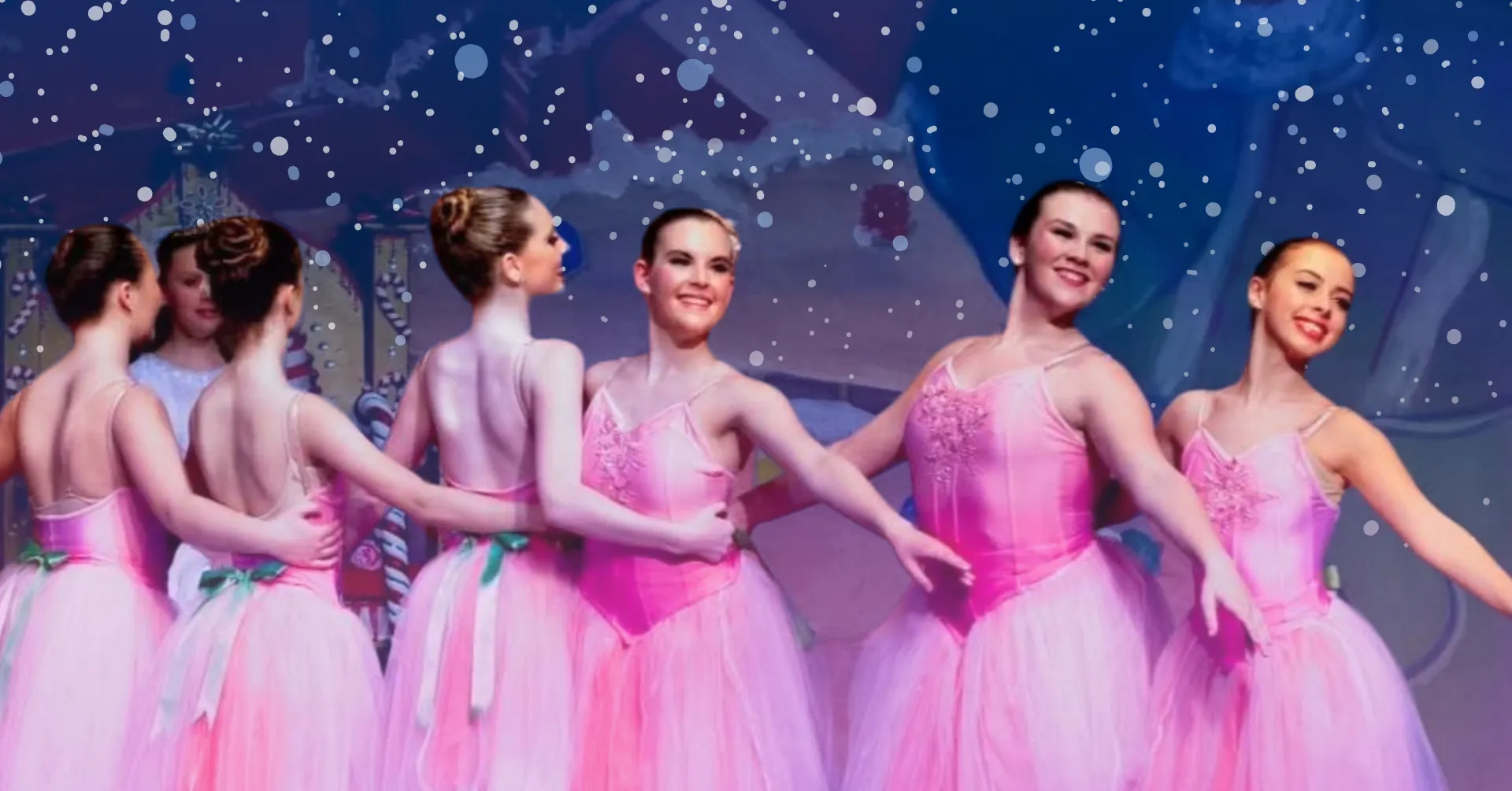 Group of young female ballerinas in pink dress costumes dance on stage with arms around one another