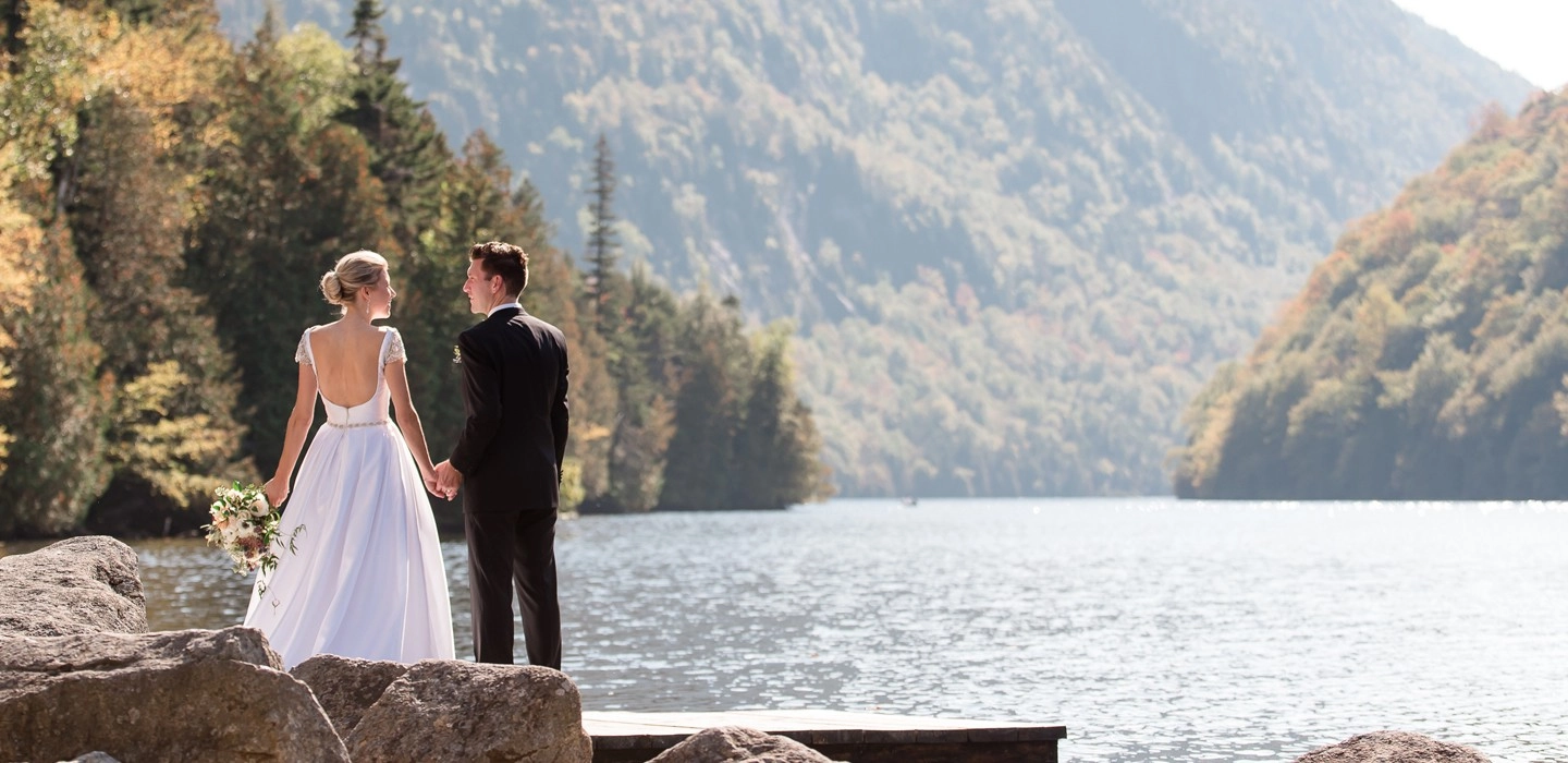 A bride and groom stand on a rocky ledge by a lake