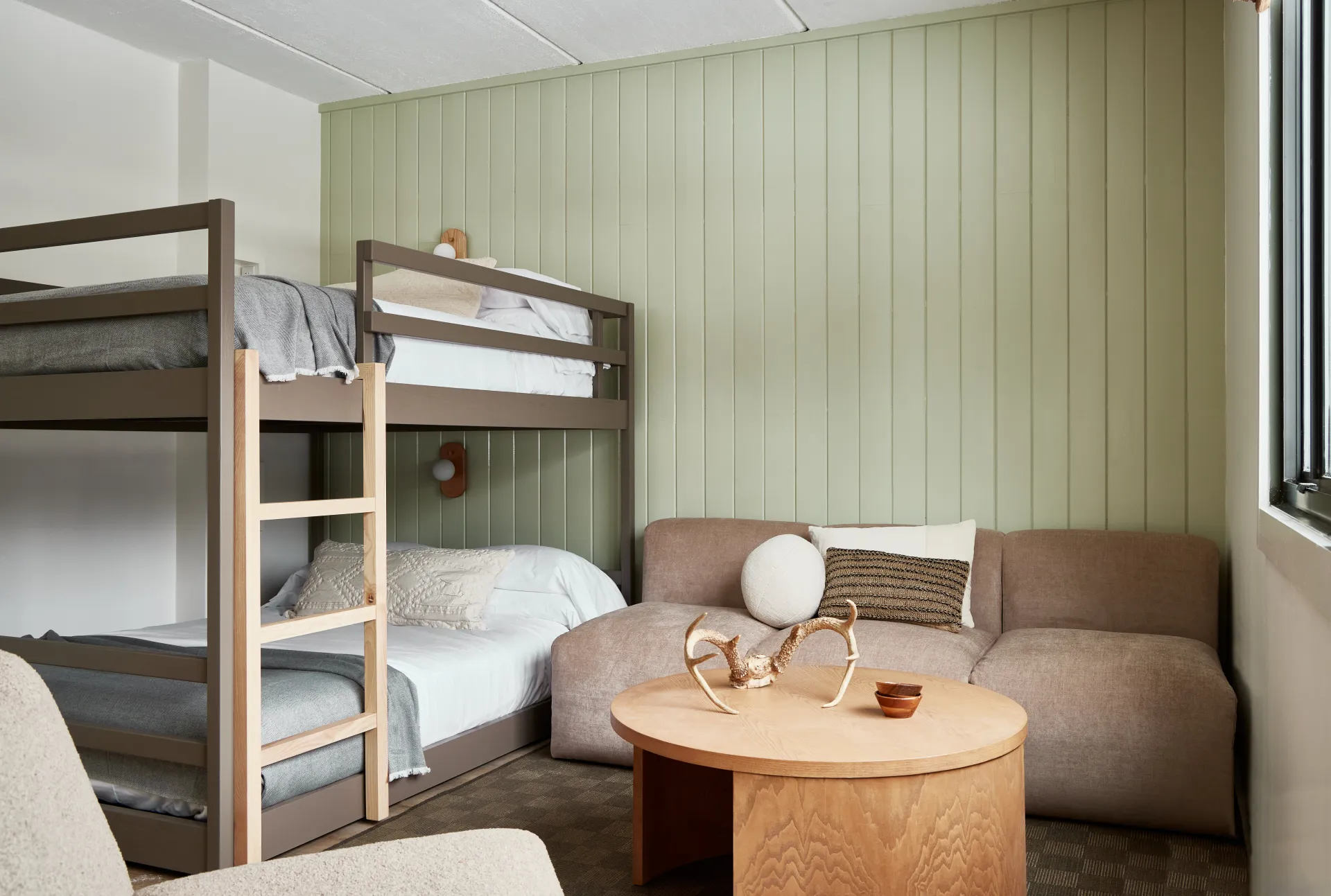 A scandinavian style bunk bed in a room with a couch and signature sculpture on the light colored coffee table.