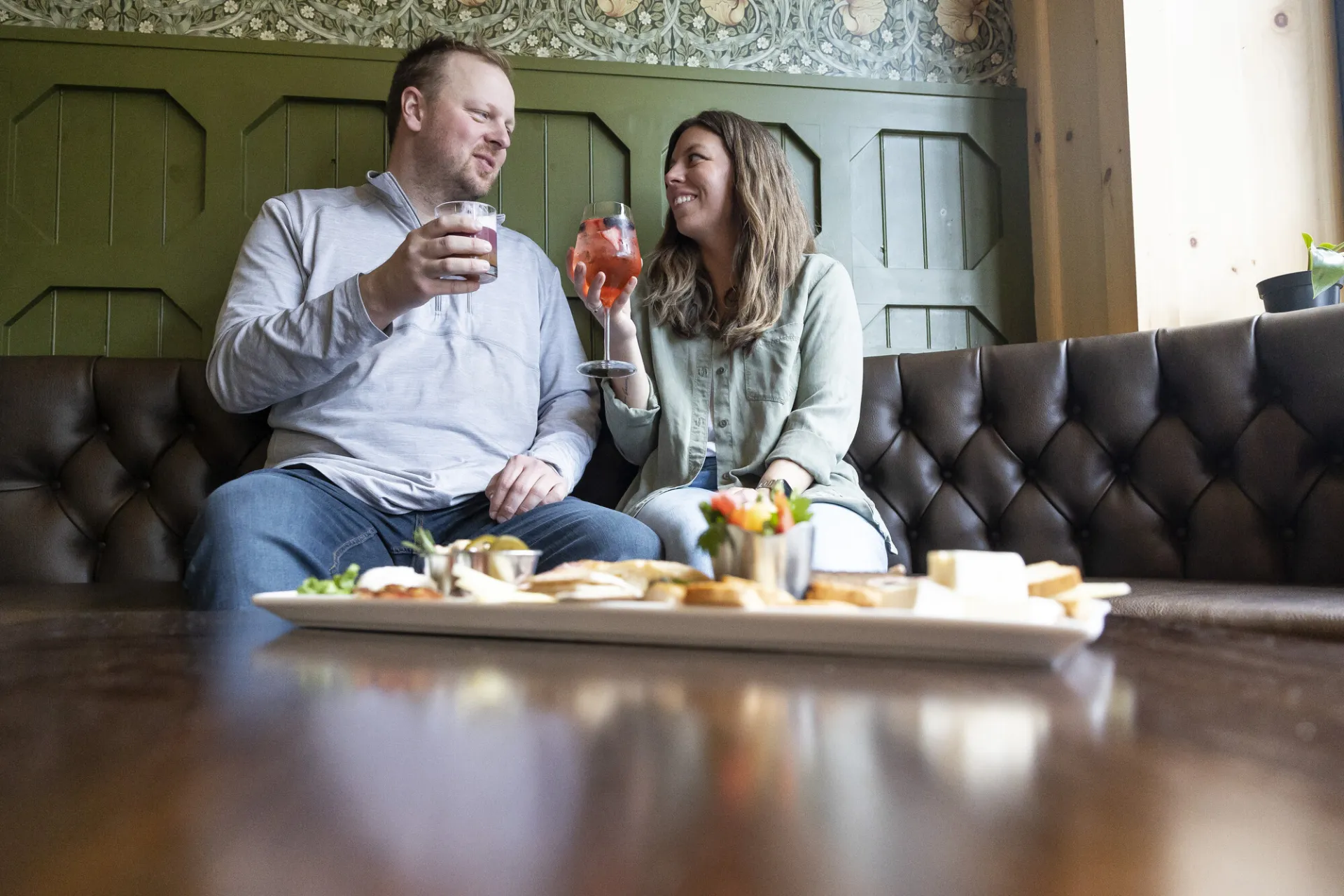 A man woman share drinks at a bar booth. 