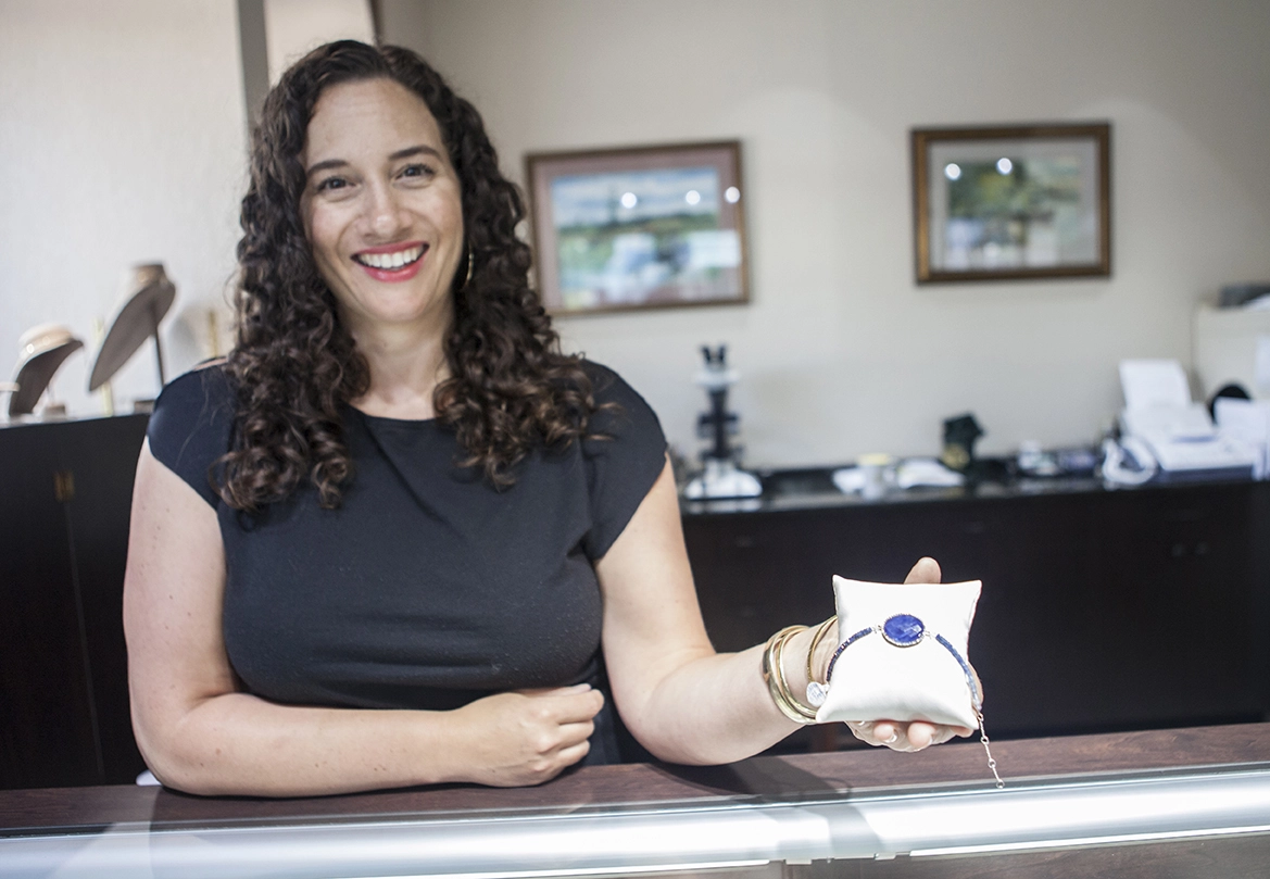 A woman holding up a piece of jewelry in a Lake Placid jewelry store.