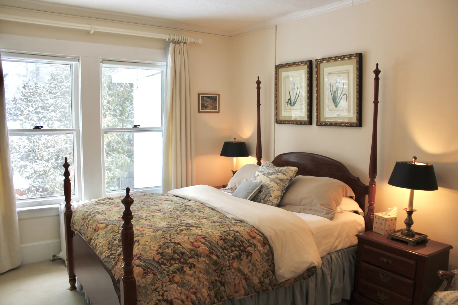 A dark four poster bed frame with light walls and intricate bedding