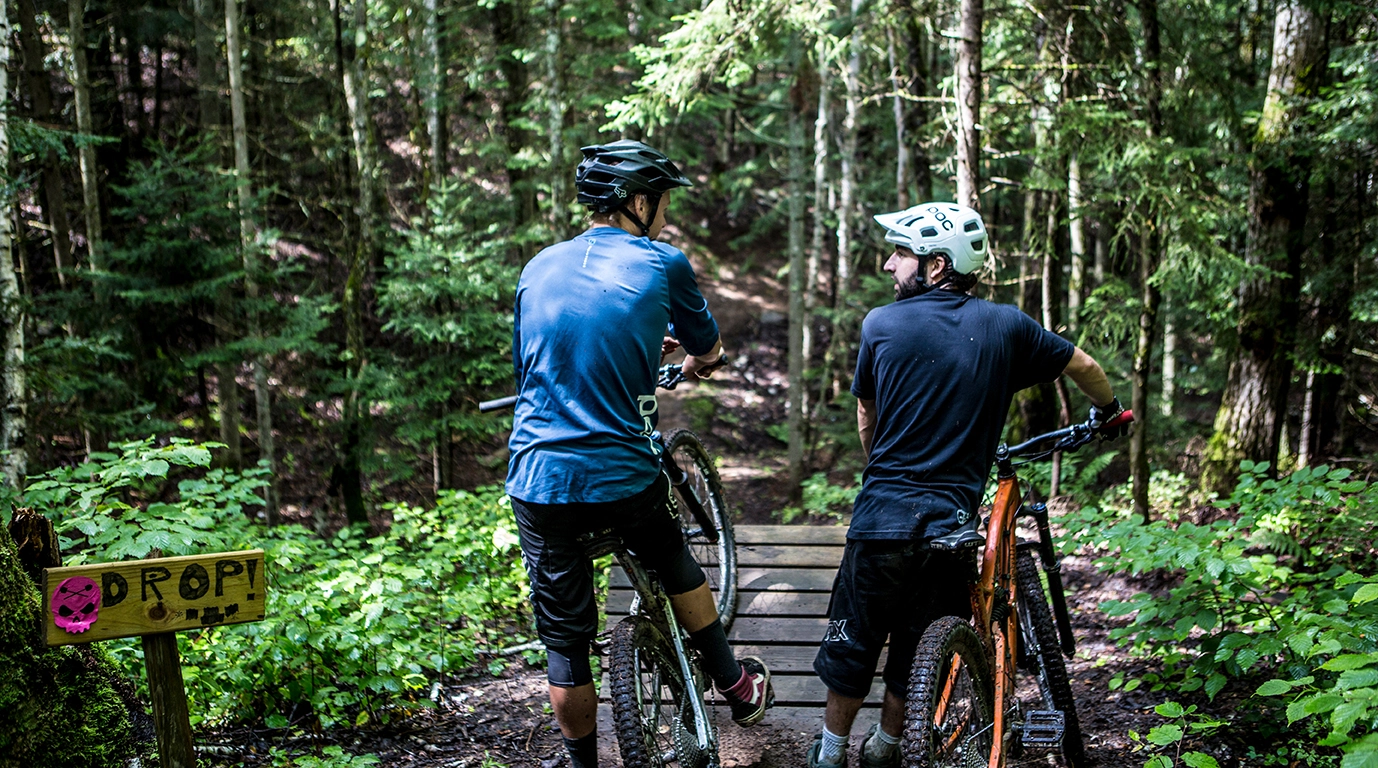 A pair of mountain bikers take a break before crossing a mountain biking bridge.