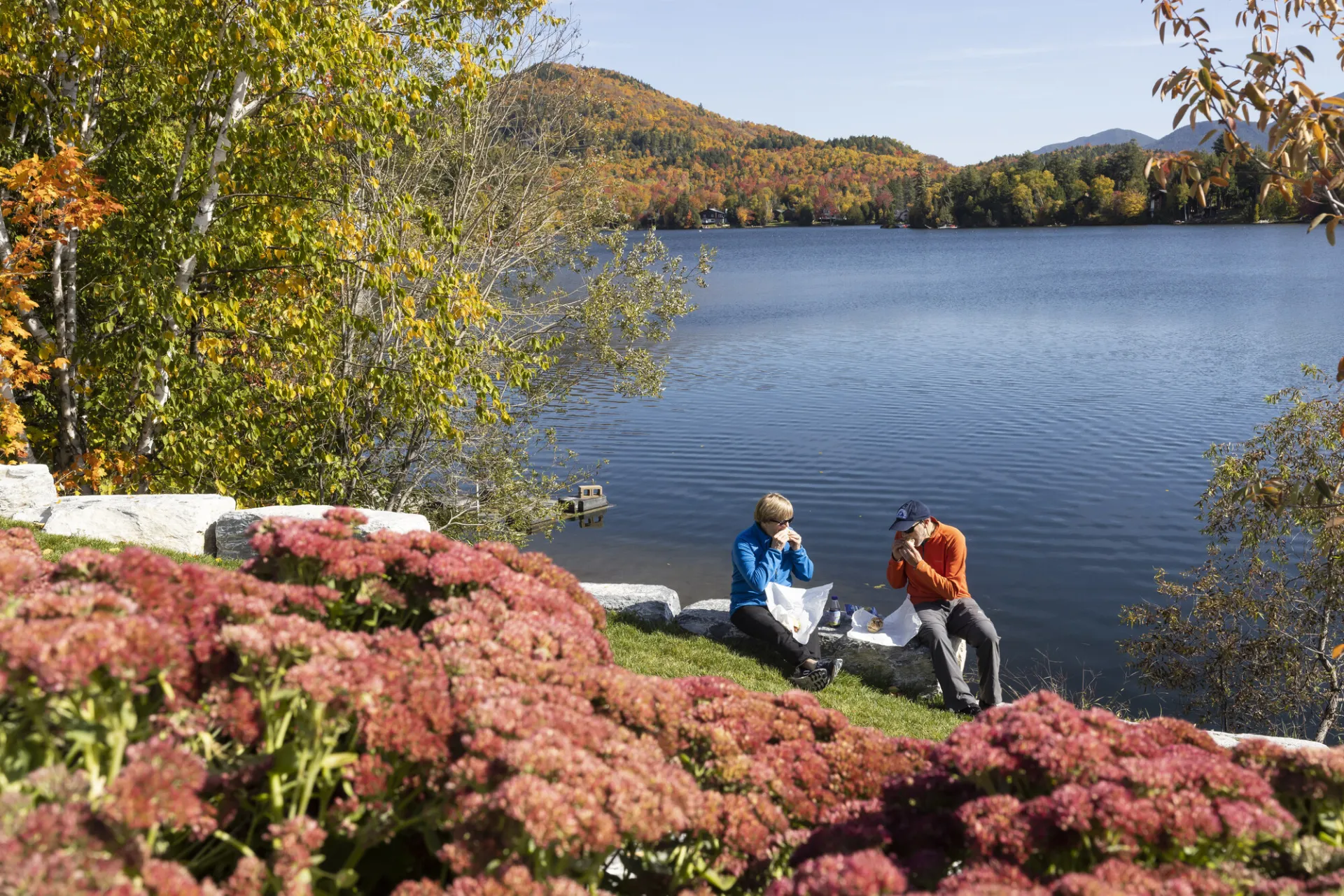 Two people eat lunch on the edge of a lake