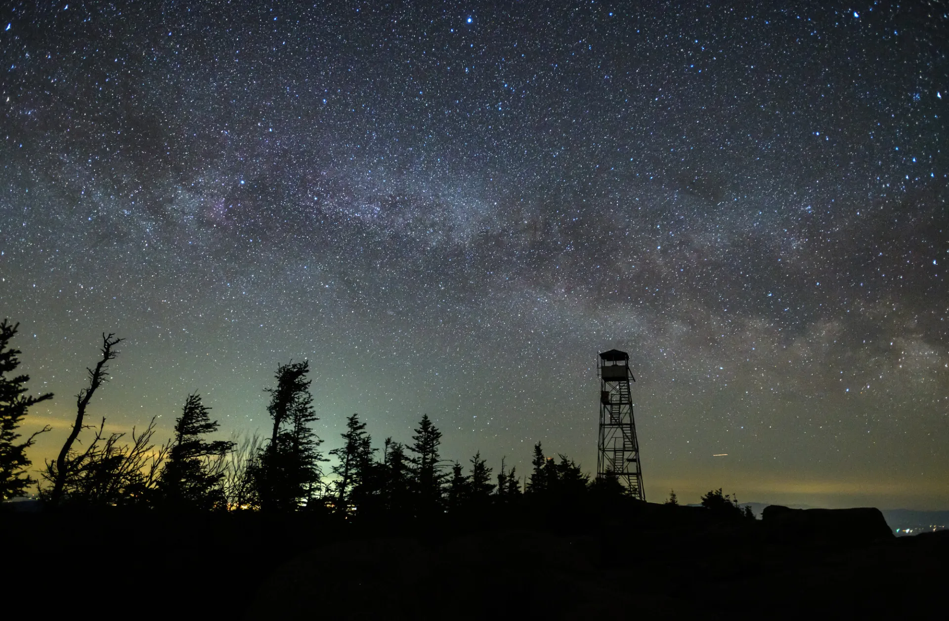 A starry night sky behind a fire tower.