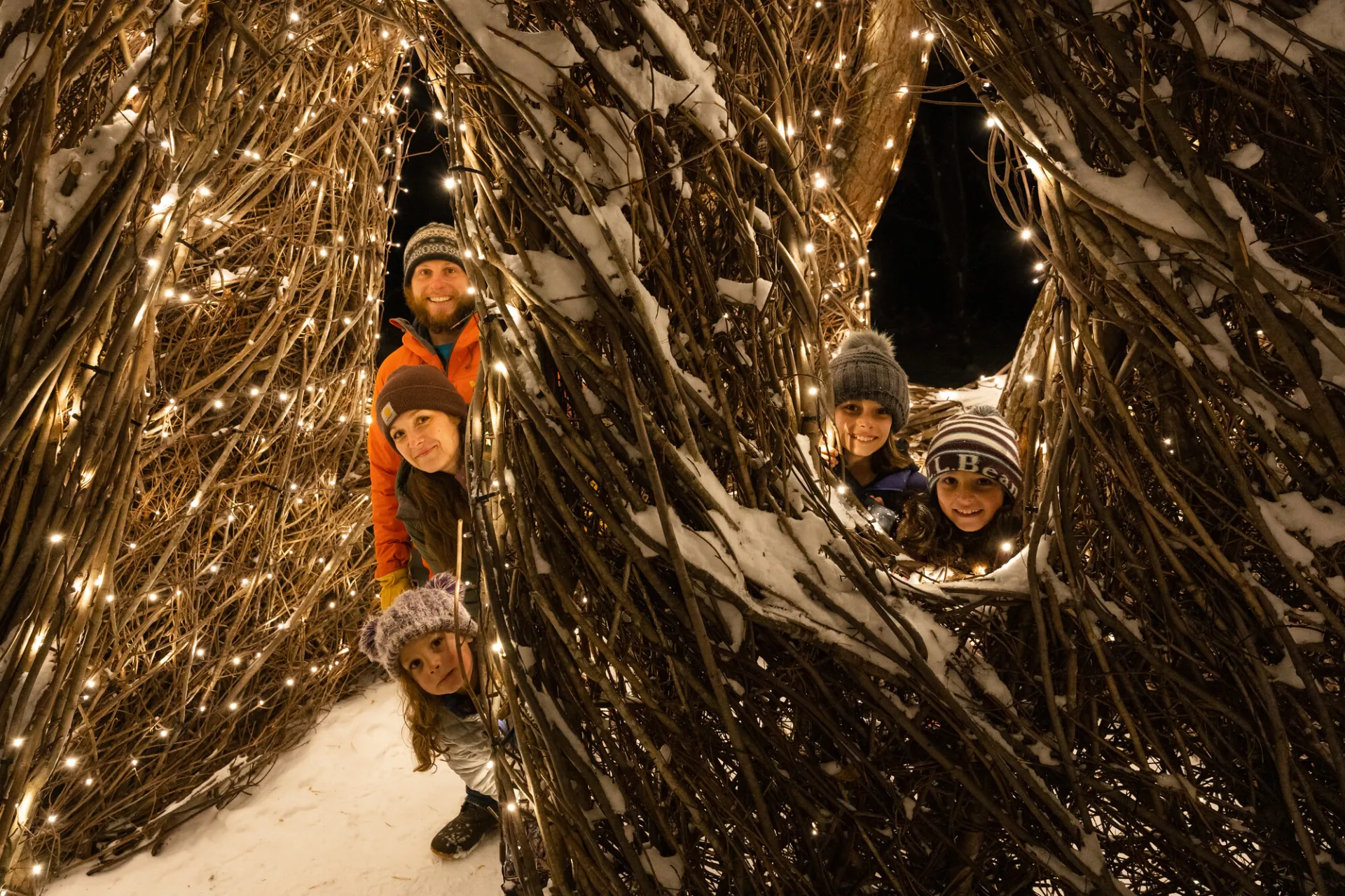 children peaking around art with christmas lights  