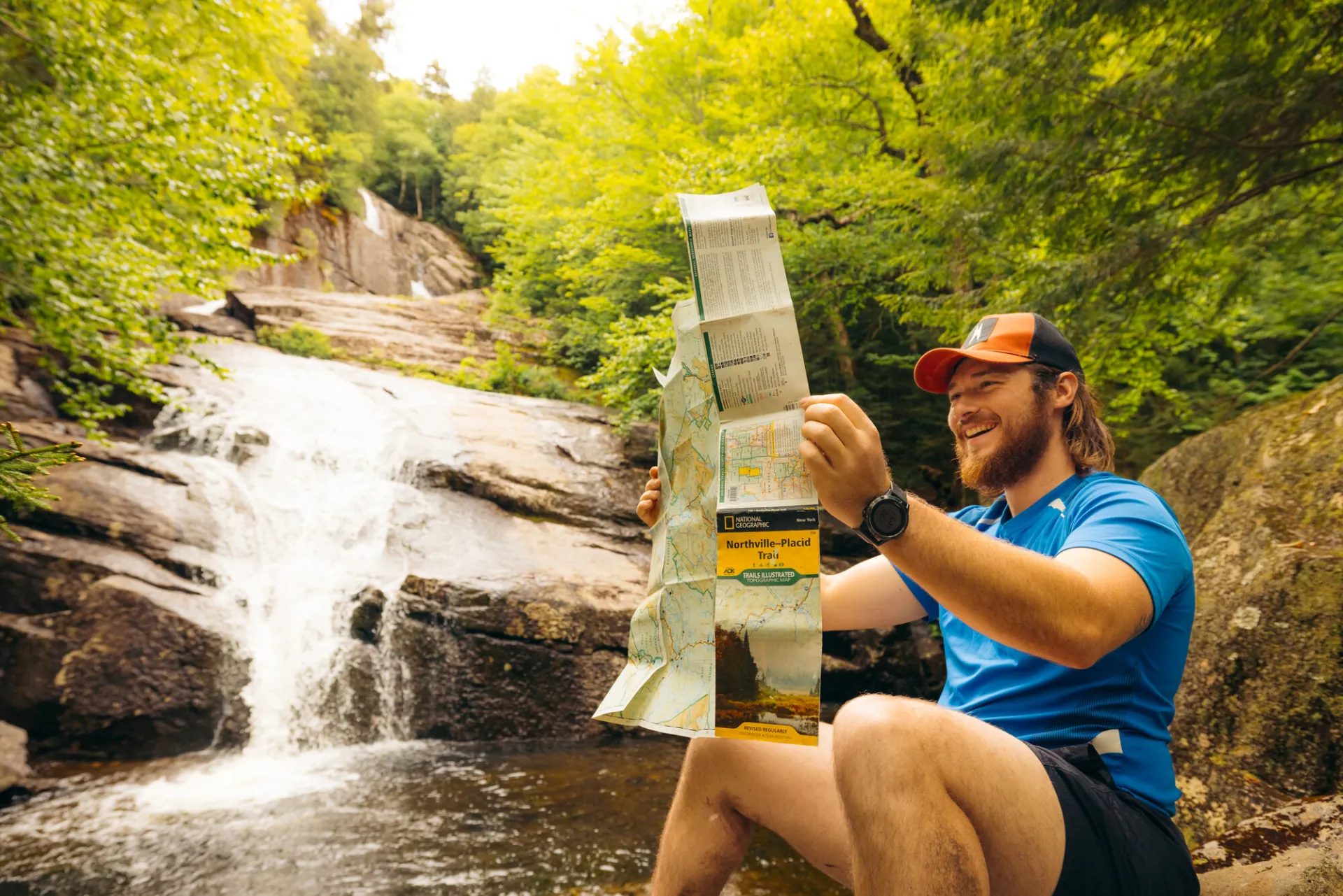 A hiker checks his map in front of a waterfall