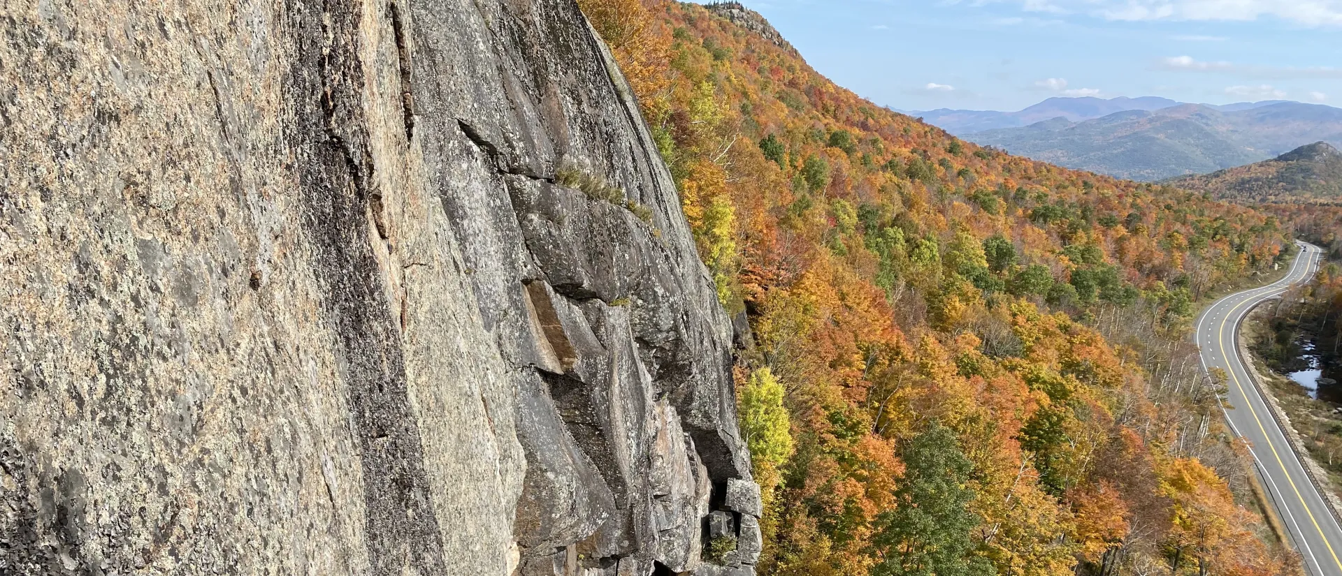 A steep rock wall with bright orange trees below