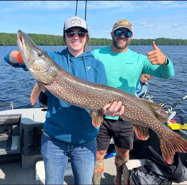 Two people holding a giant pike while giving thumbs up.