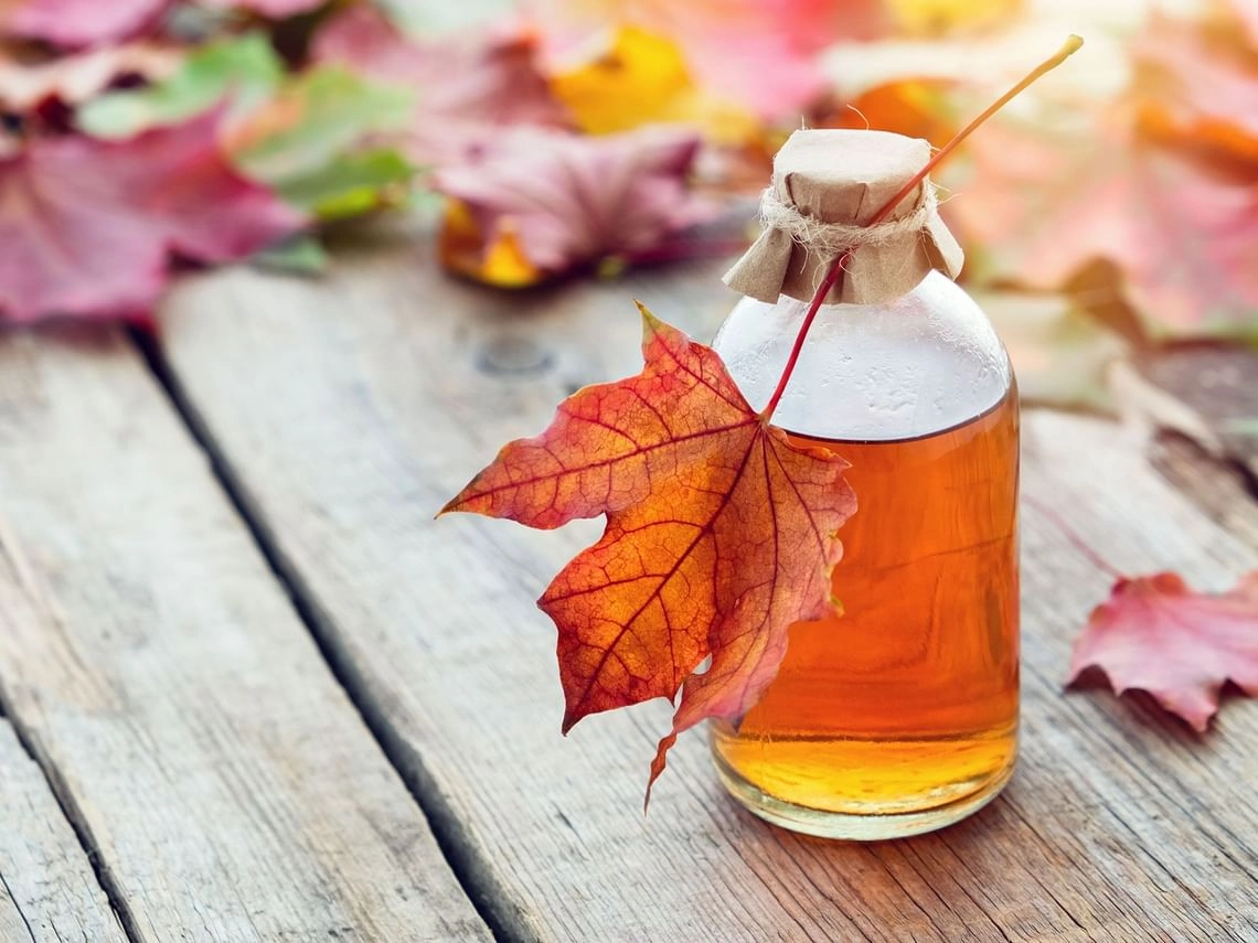 A small jar of maple syrup surrounded with fallen leaves and tied with jute twine