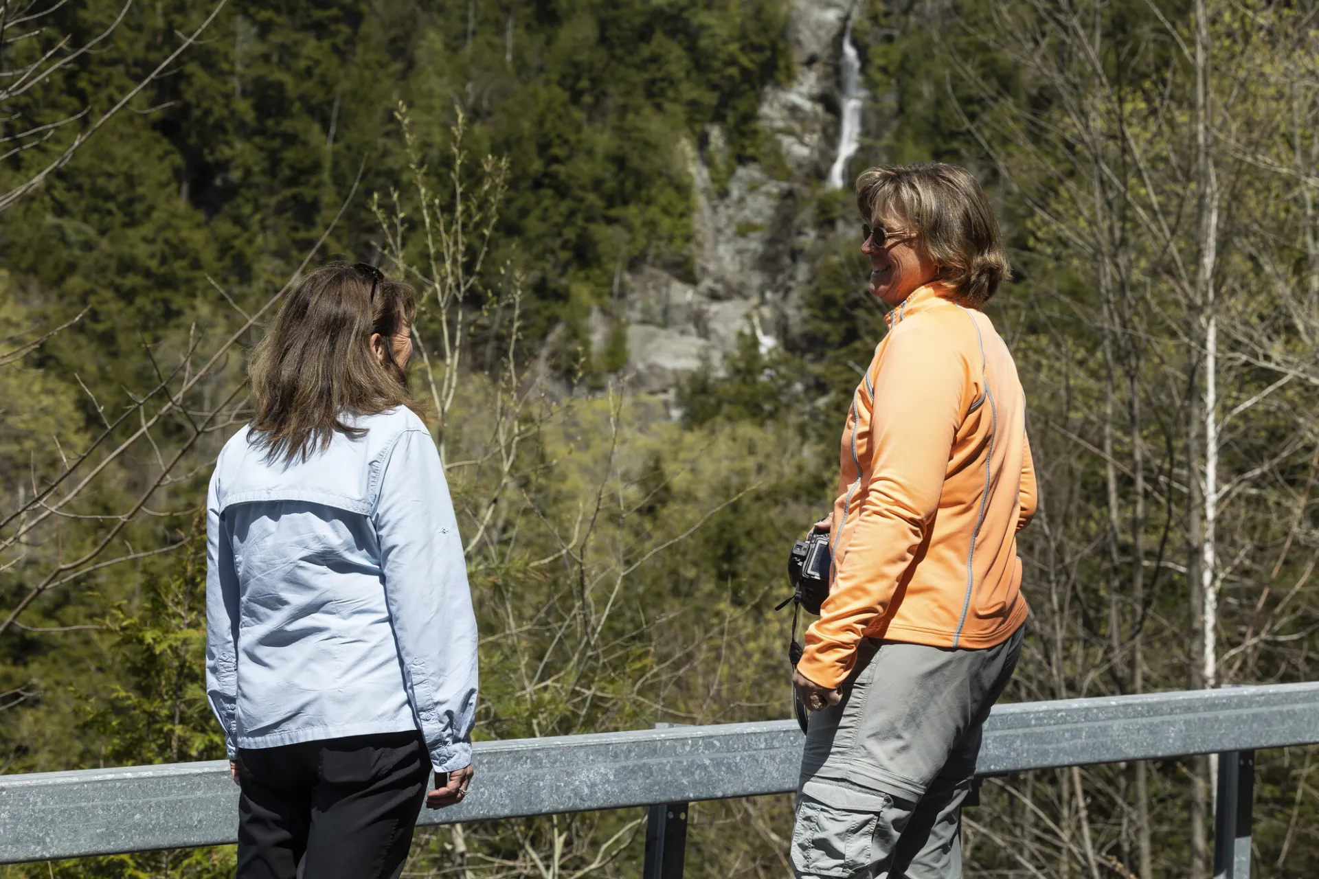Two woman standing on the side of the road in front of a waterfall