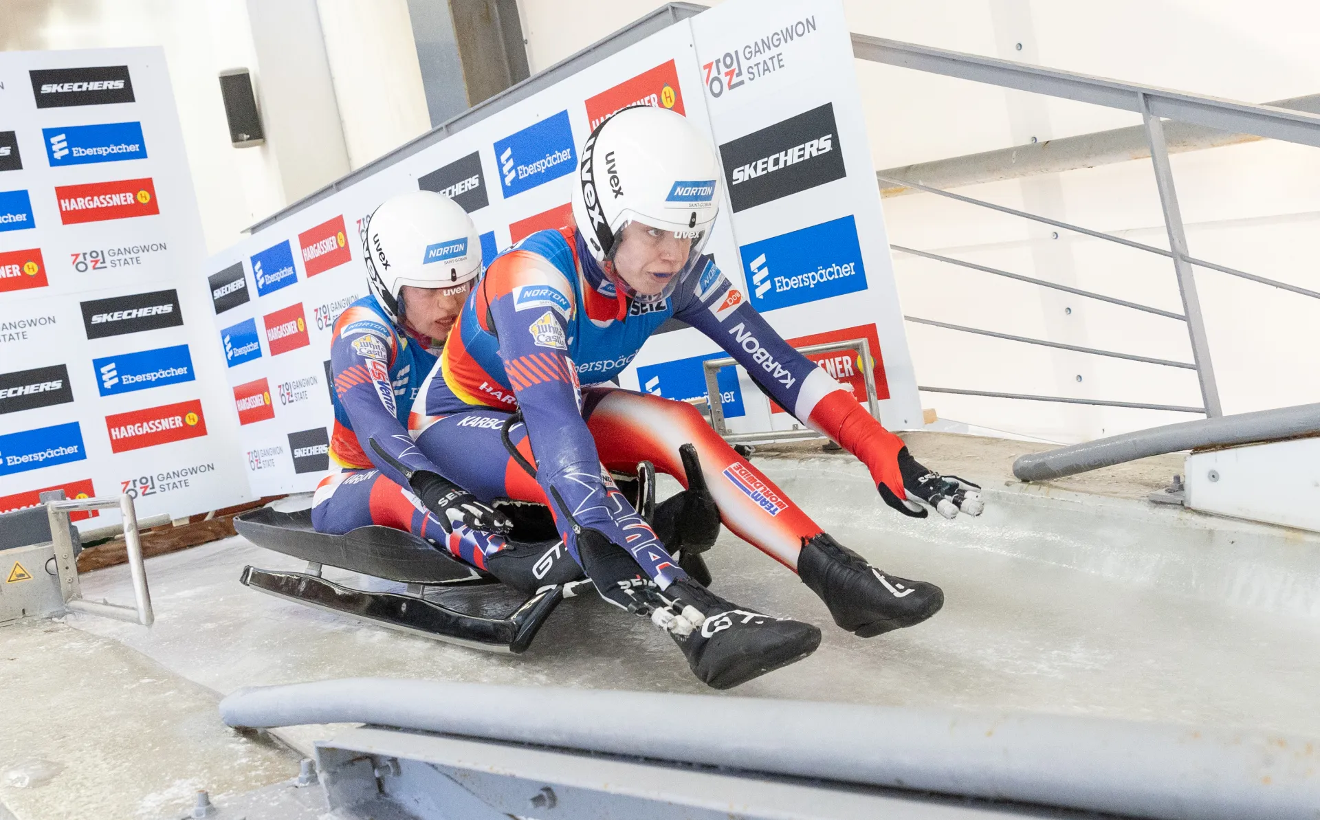Two women's doubles luge athletes racing down an icy track.