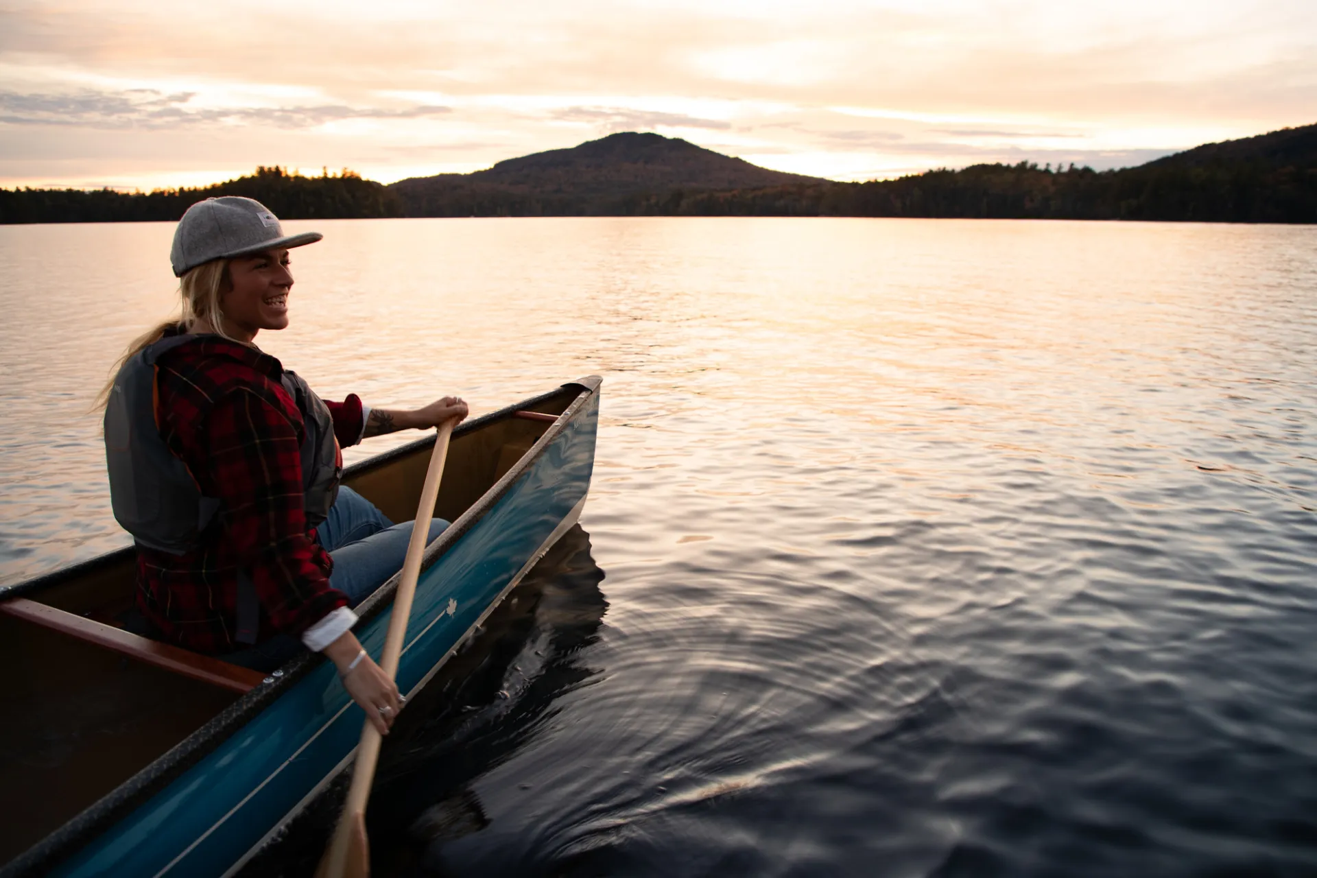 A woman paddling a canoe on a lake during sunset.