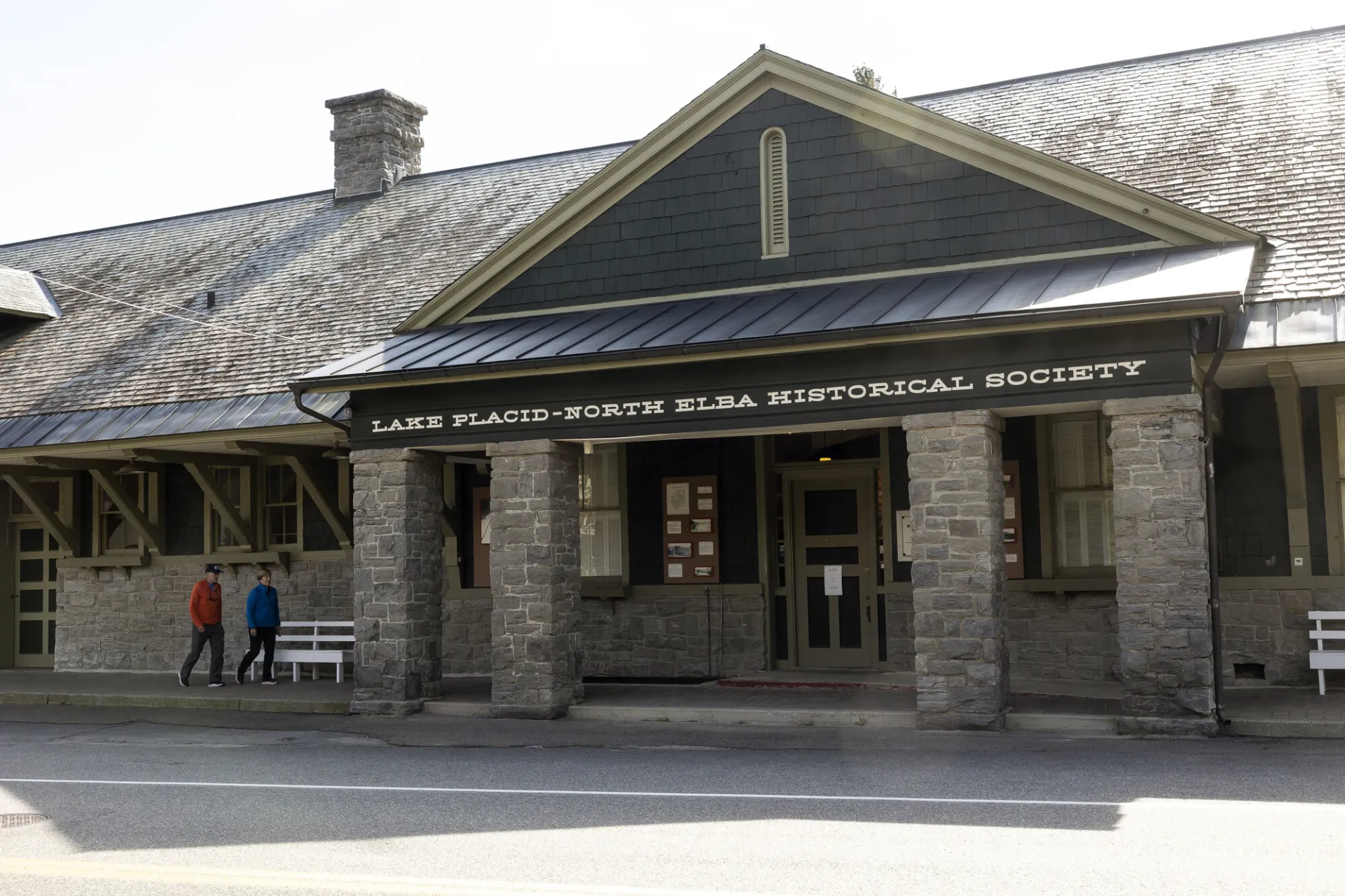 Two people walk on covered walkway up to the doors of the Lake Placid–North Elba Historical Society & Museum