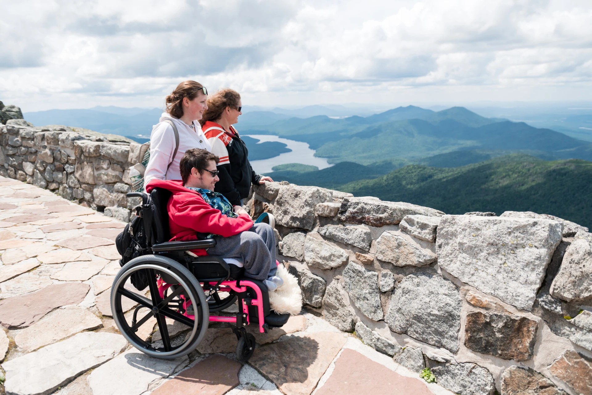 A smiling wheelchair user look out at the view from the observation patio on the very top of Whiteface Mountain.
