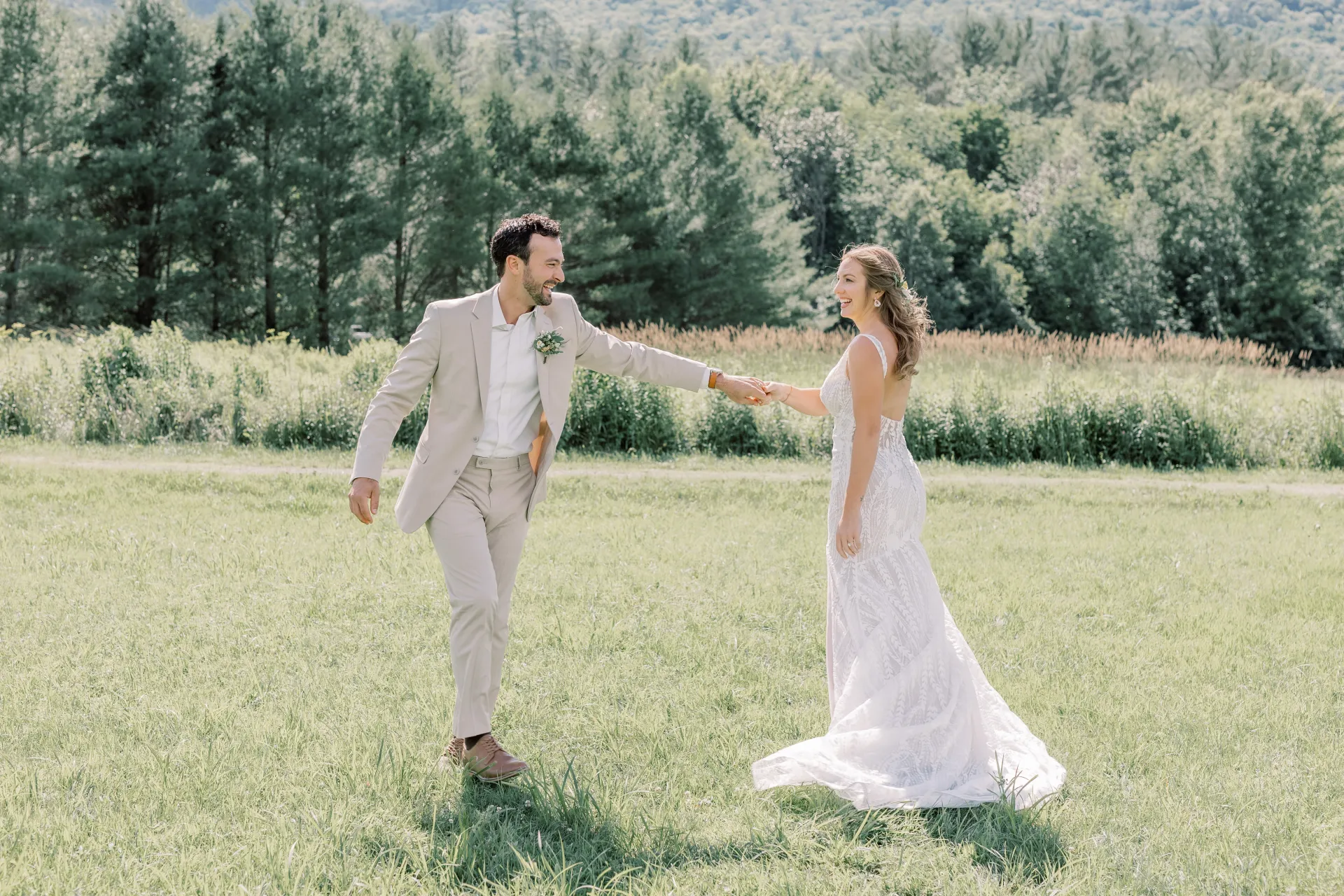 Bride and groom laugh and dance in a grassy field
