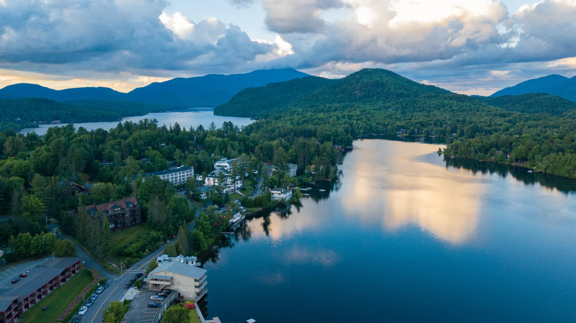 An aerial view of a town on a lakeshore. More lake and mountains are in the distance.