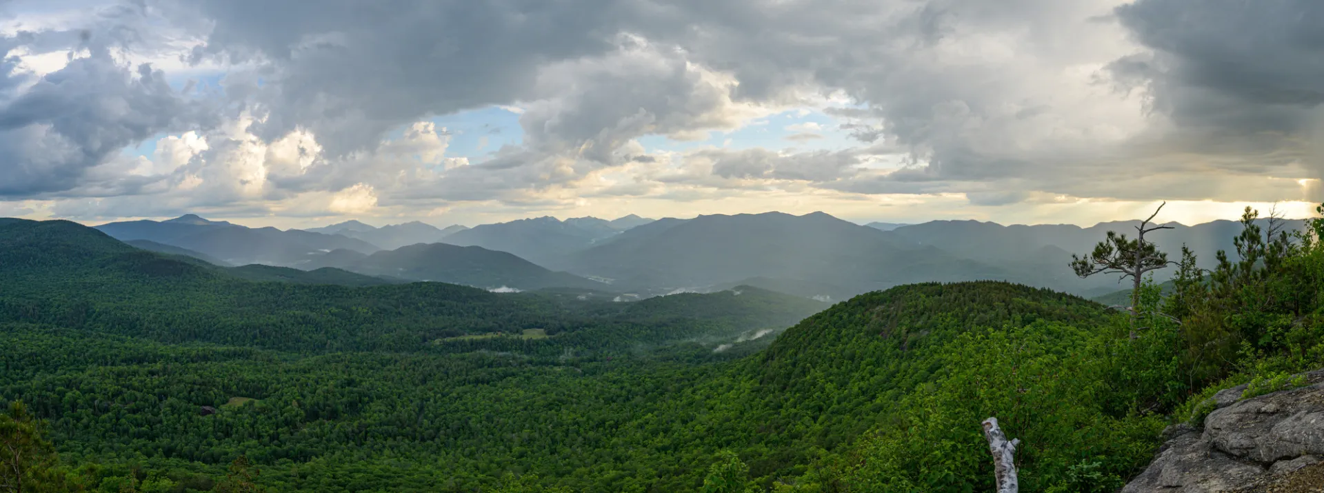 A view from the summit of a mountain with clouds and summer mountain views.