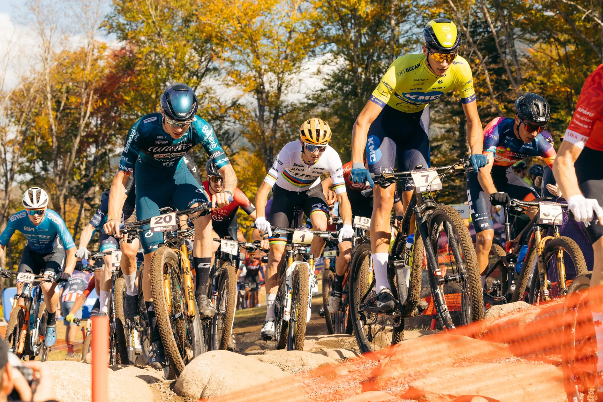 Pack of mountain bikers in colorful uniforms racing on dirt trail