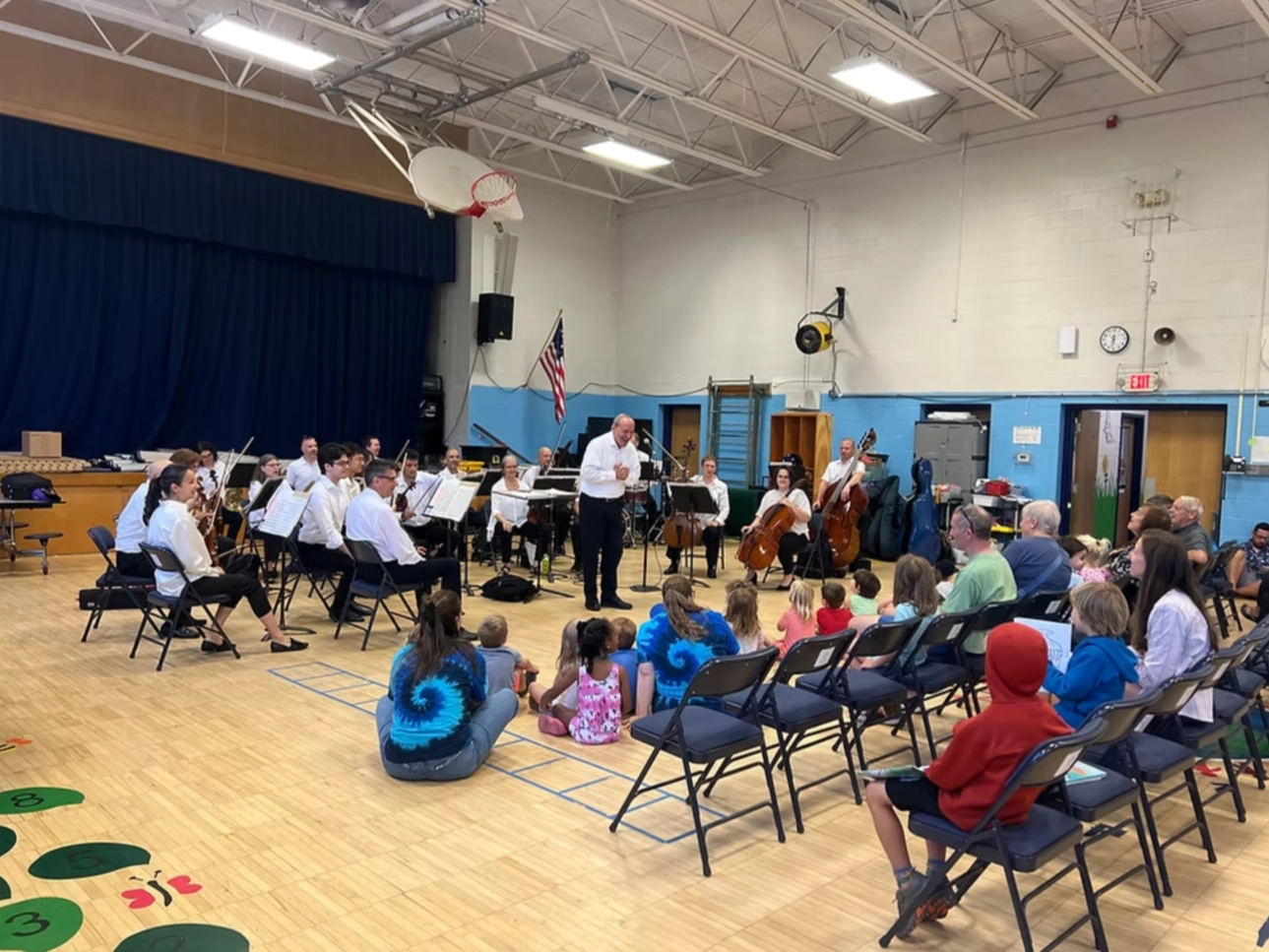 Lake Placid Sinfonietta set up in gym of school with children and parents sitting on floor and in rows of folding chairs