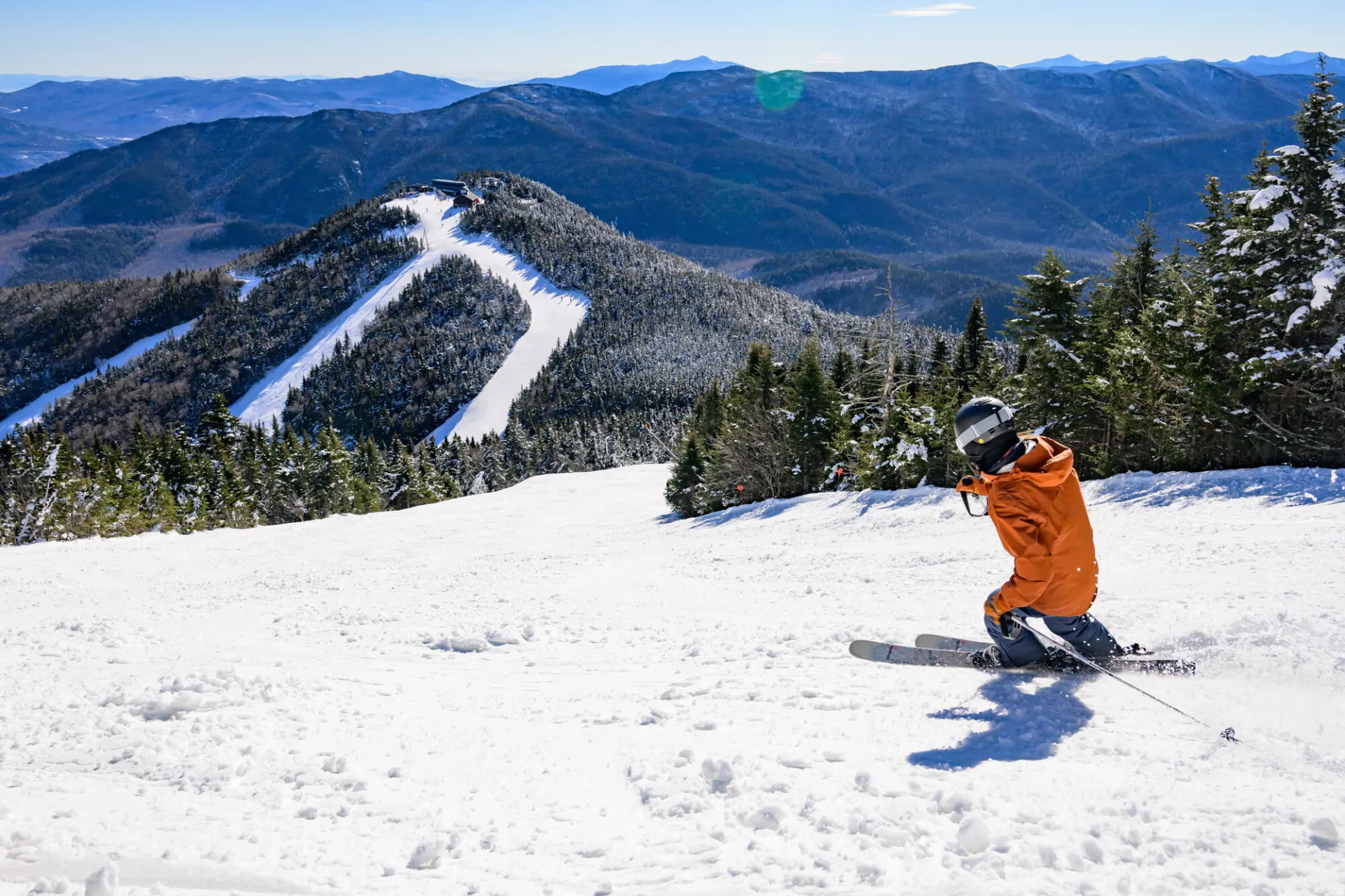 A man in an orange jacket skis down a mountain in winter. 