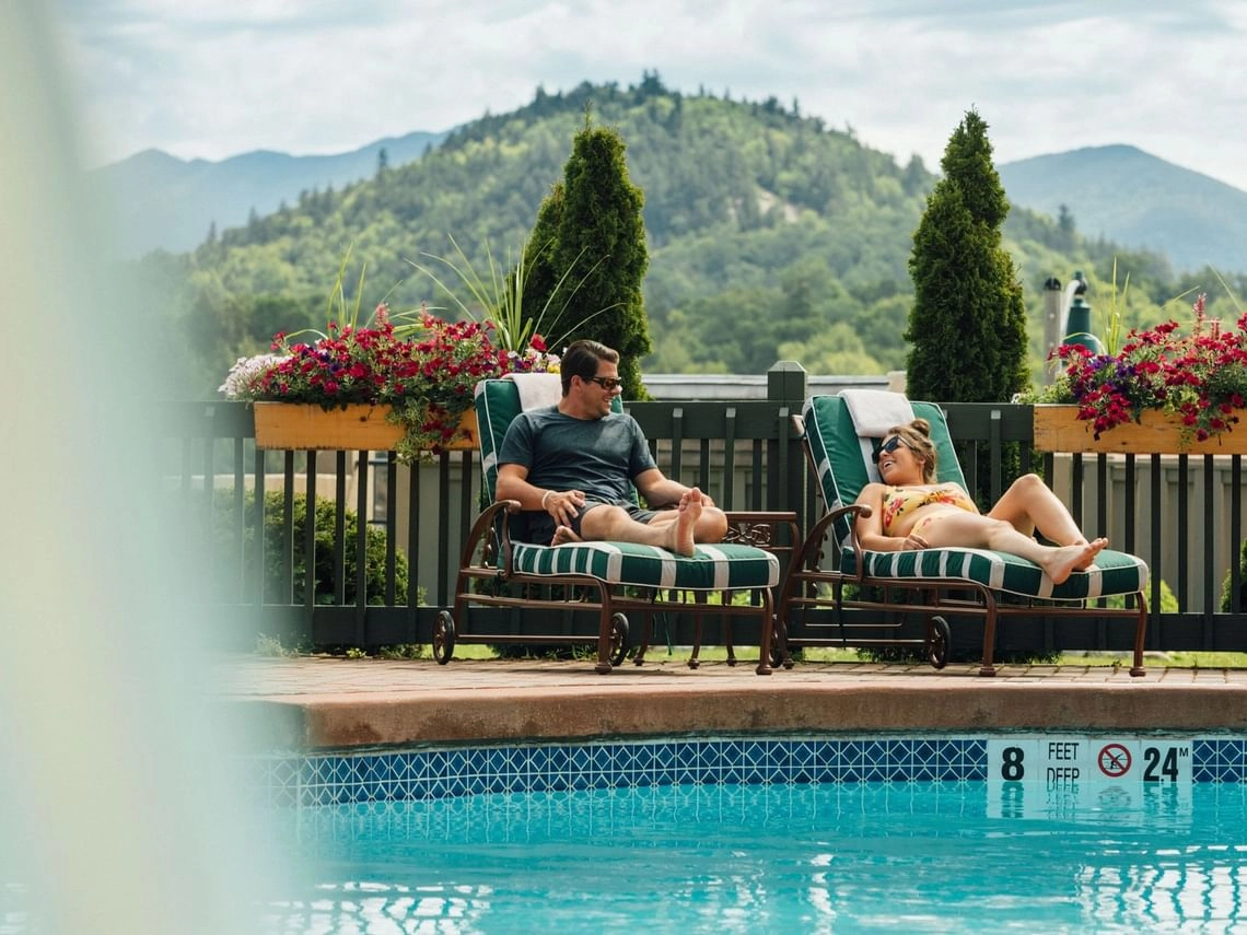 A couple lounges by the outdoor pool with the mountains in the distance
