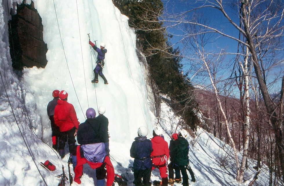 A group of climbers stand and watch a climber ascend the ice.