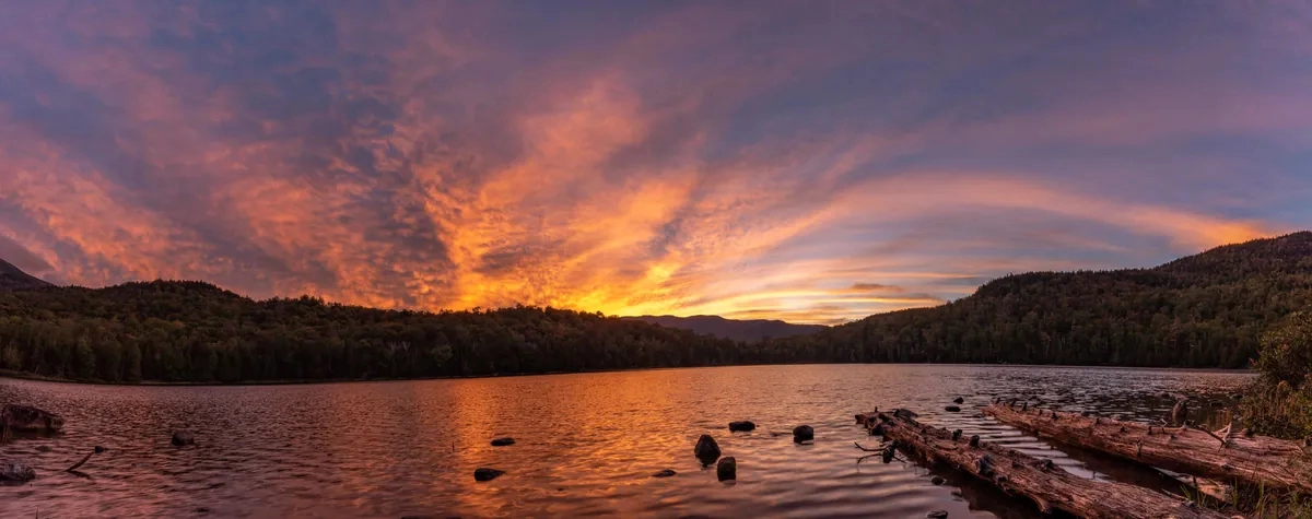 Sunset over a rocky lake ranging from reds and oranges through golds and yellows to purples all the way to the deep blue sky.