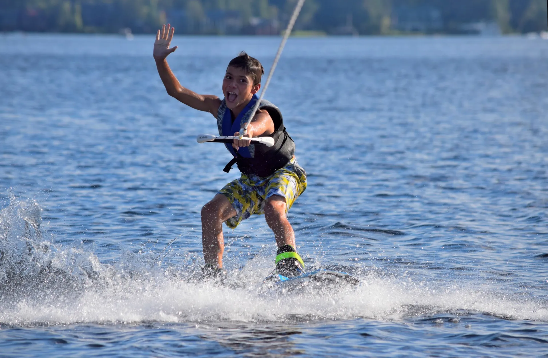 A wake boarder waves to camera.