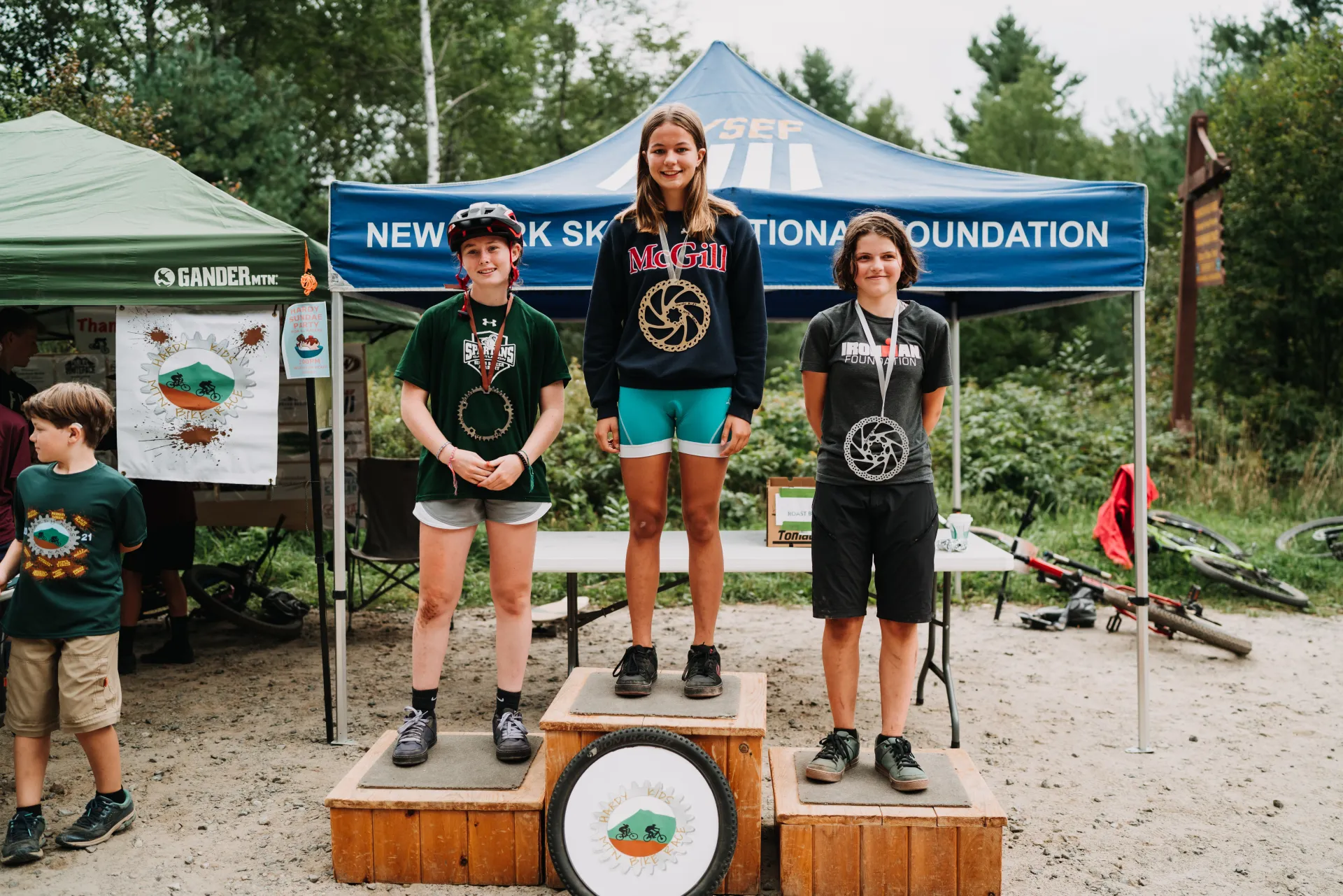 Three kids stand atop podium with medals at mountain biking event