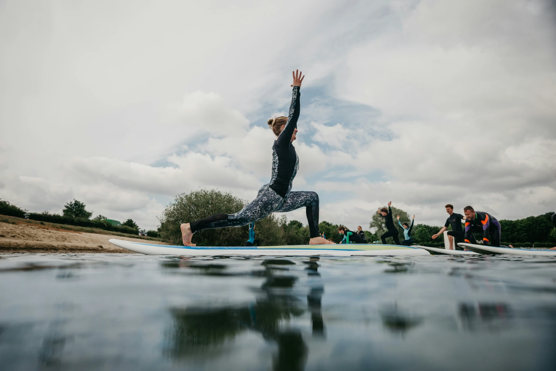 Stock image of person striking yoga pose on stand up paddle board on water with other paddlers mirroring