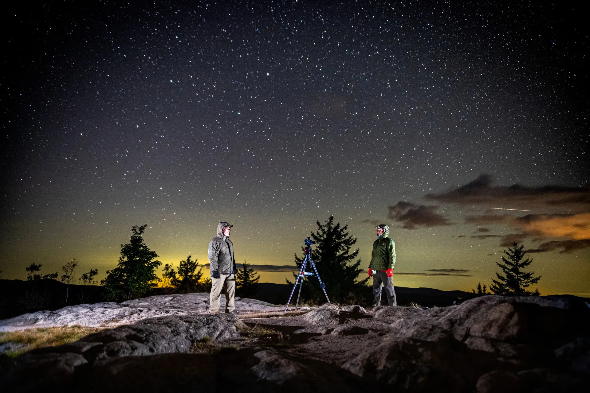 Two hikers photographing the night sky at the top of a summit.