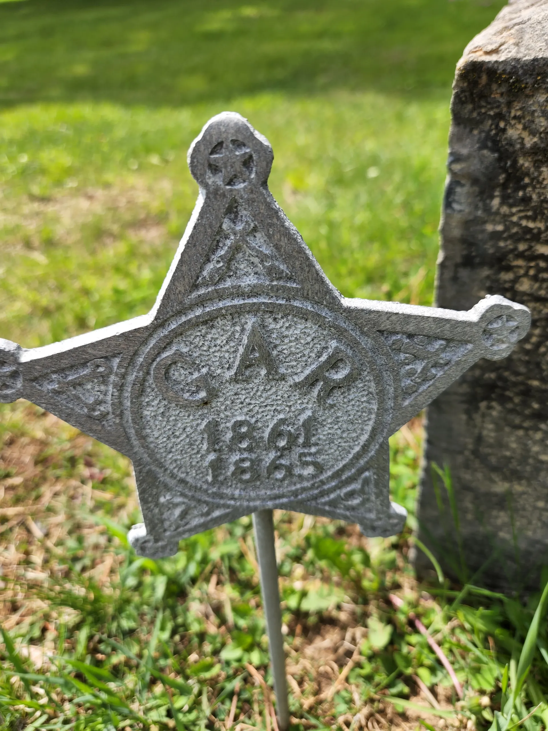 A cast metal civil war memorial star: GAR 1861-1865, on a short post by a gravestone