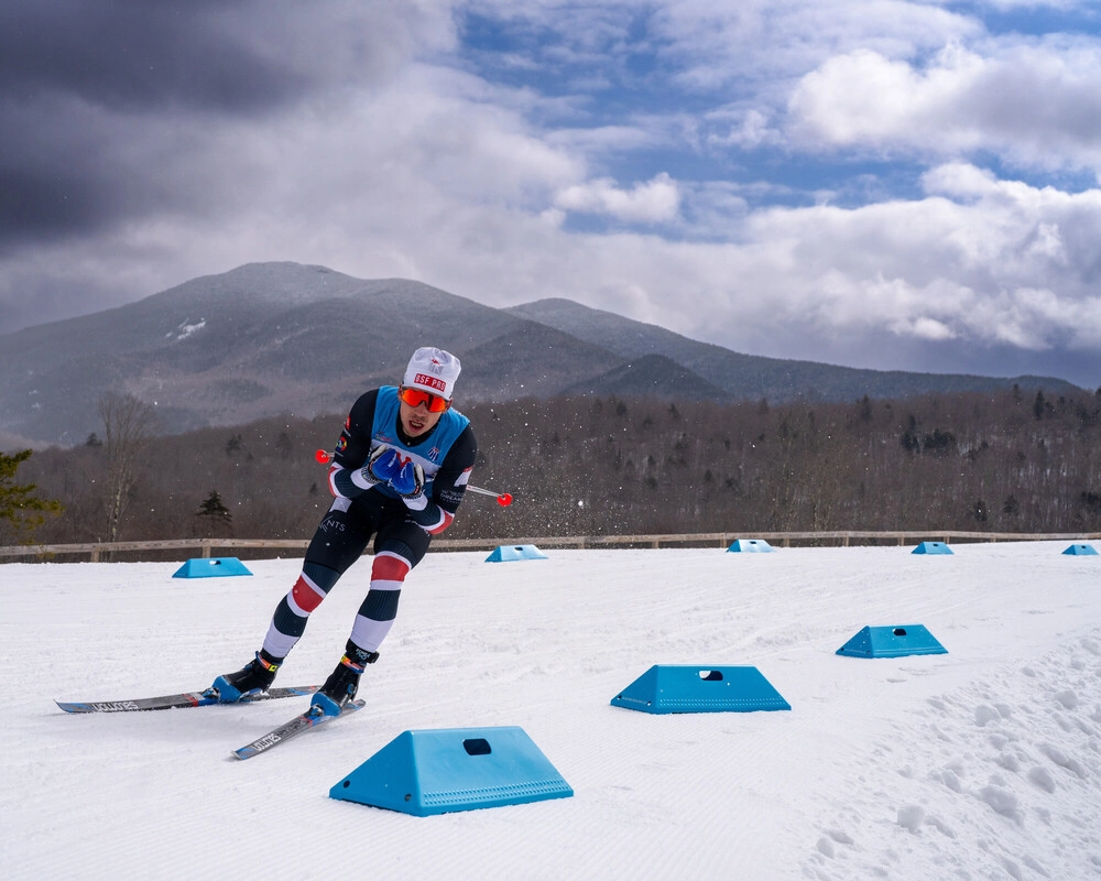 A skier in a blue and red outfit navigates a snowy course marked by blue obstacles. 
