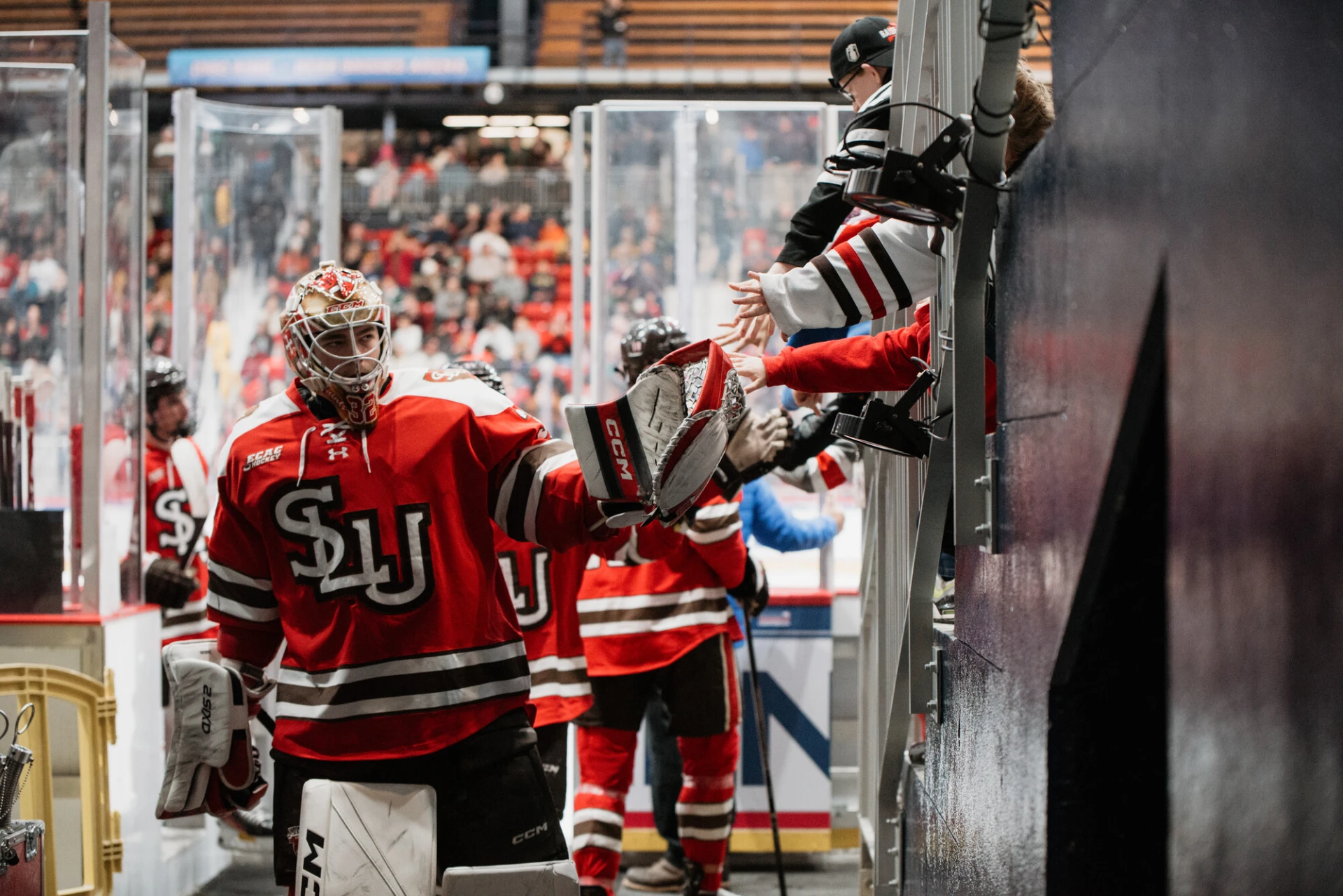 St Lawrence University hockey players give high fives and fist bumps to hands reaching over partition as they leave the ice 