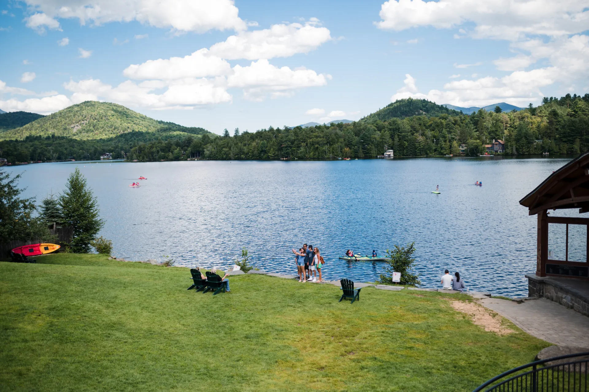 A sunny summer day at a green park with lake and mountains in the background.