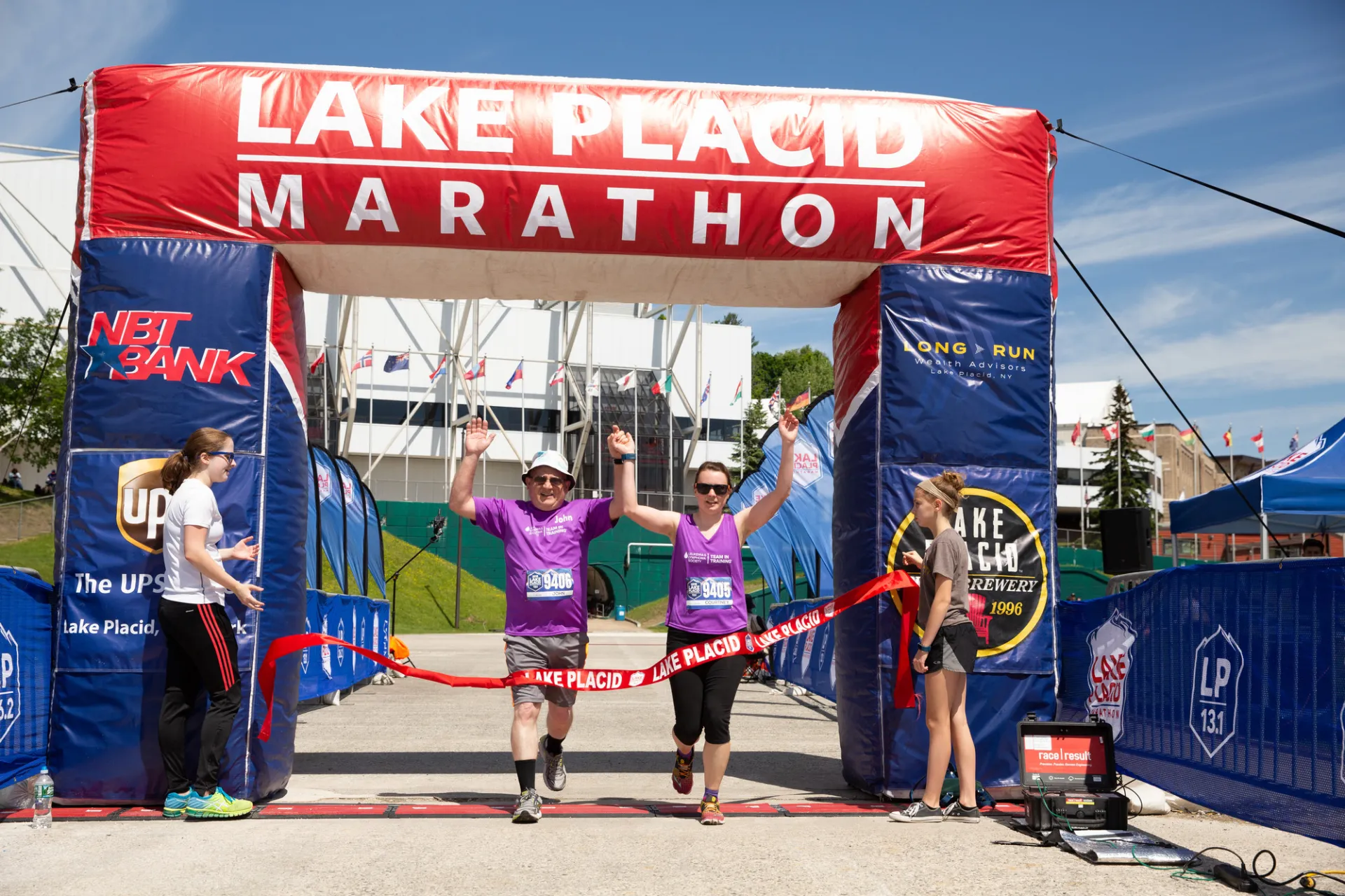 Two athletes cross the finish line holding hand in the air