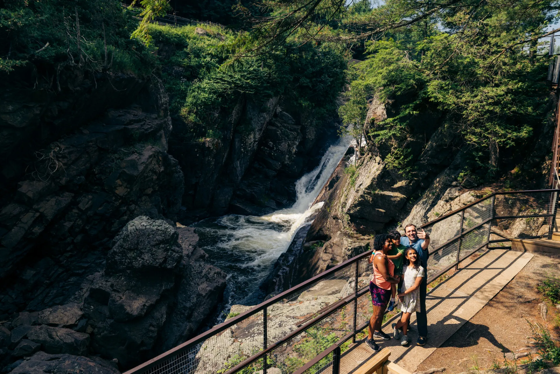 Two adults and a child pose for a selfie in front of a rocky chasm on a sunny summer day.