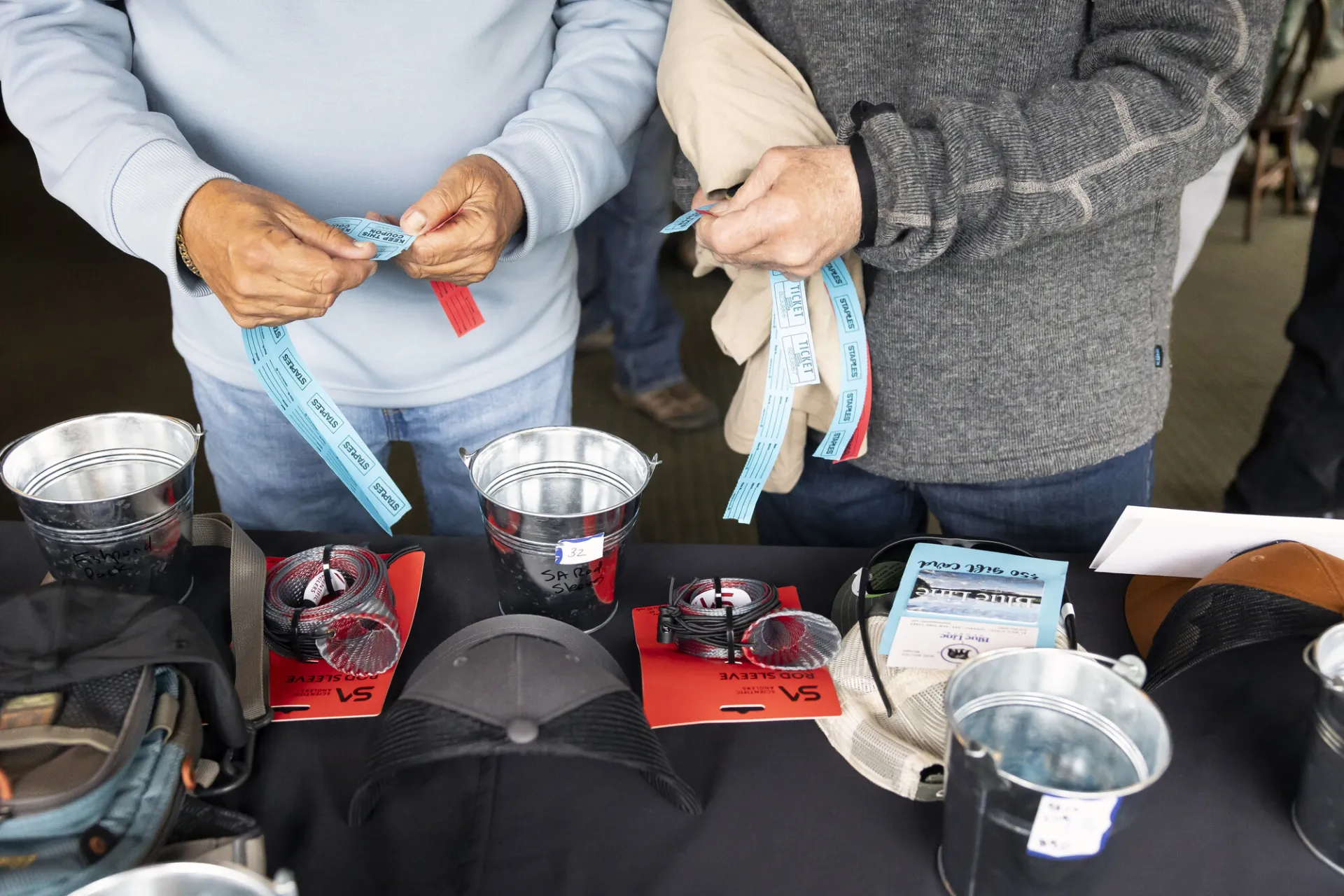 Two peoples' hands seen tearing raffle tickets at table of fly fishing raffle items at Two-Fly Challenge event