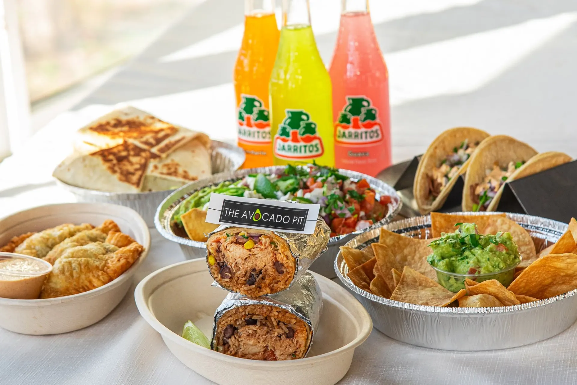 An assortment of bowls of nachos, burritos, tacos and Mexican flavors of sodas.