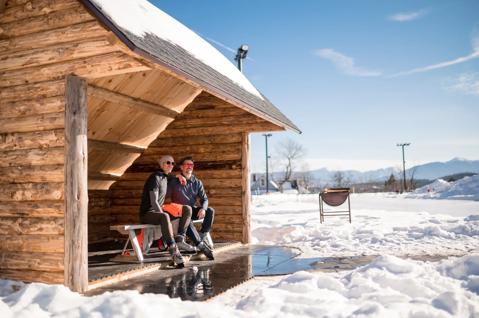 A snow covered lean to with the mountains in the distance.