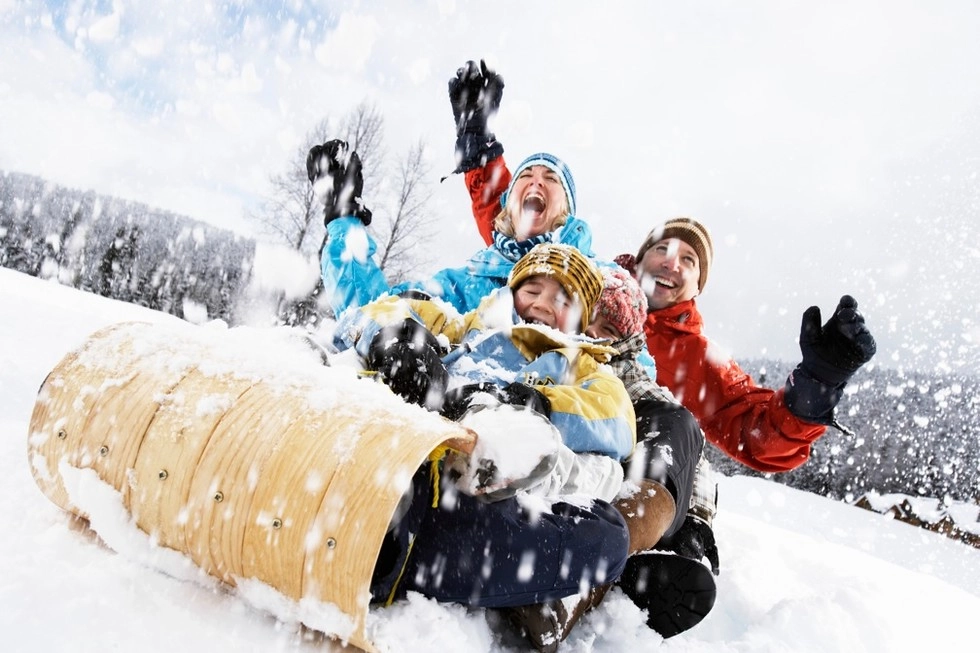 A young family  laughs their way down the sledding hill on a tobogan as the snow flies around them