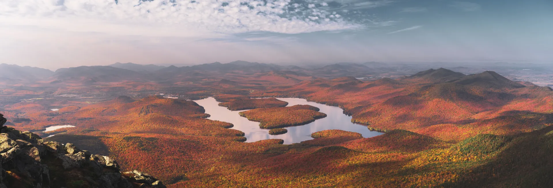 View from elevation of Lake Placid surrounded by forested shoreline bright with fall colors