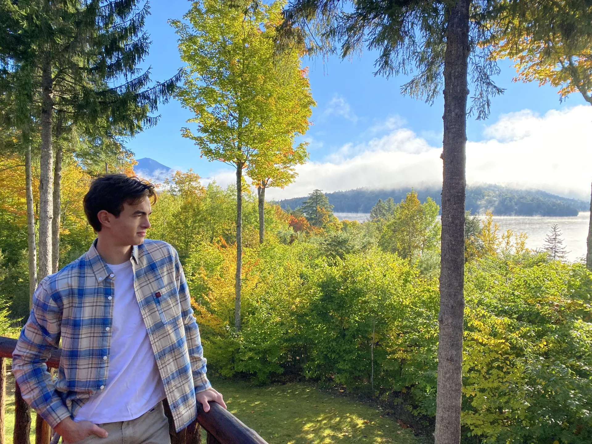 A young man in a flannel looks out over the trees and mountains.