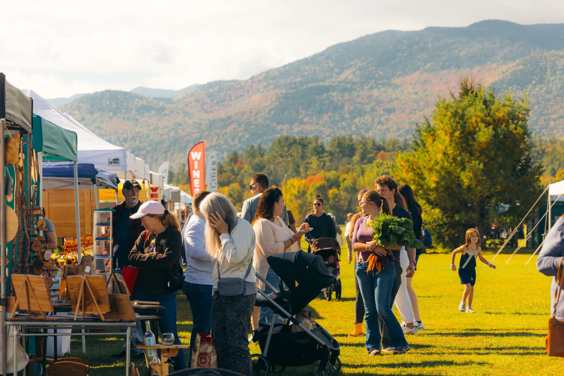 People browse various farmers market vendors and walk between rows of tents with mountains in background