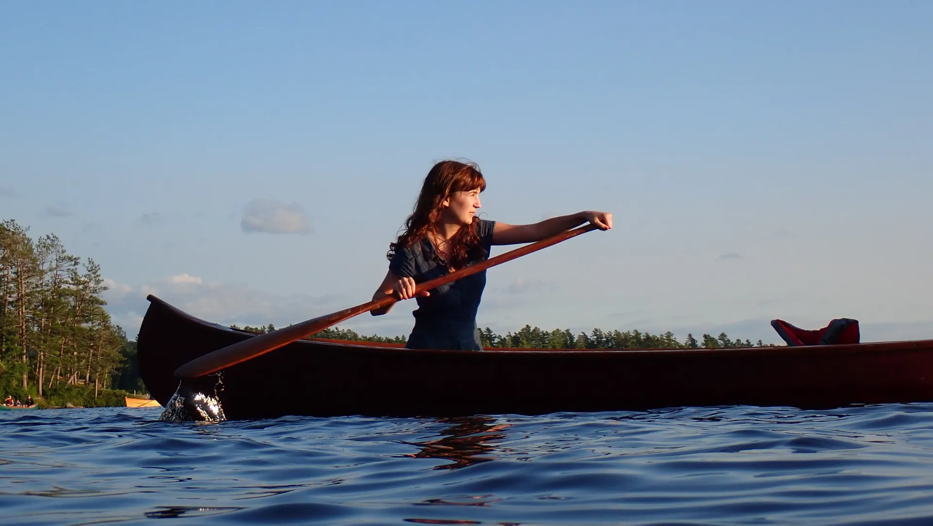 A red headed woman in a blue dress paddles  her canoe