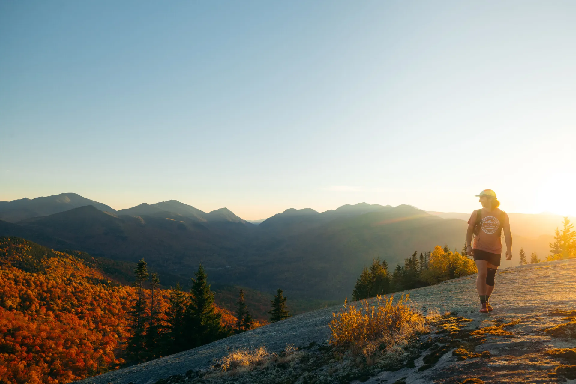 A man walks on the rocky top of a mountain during fall.