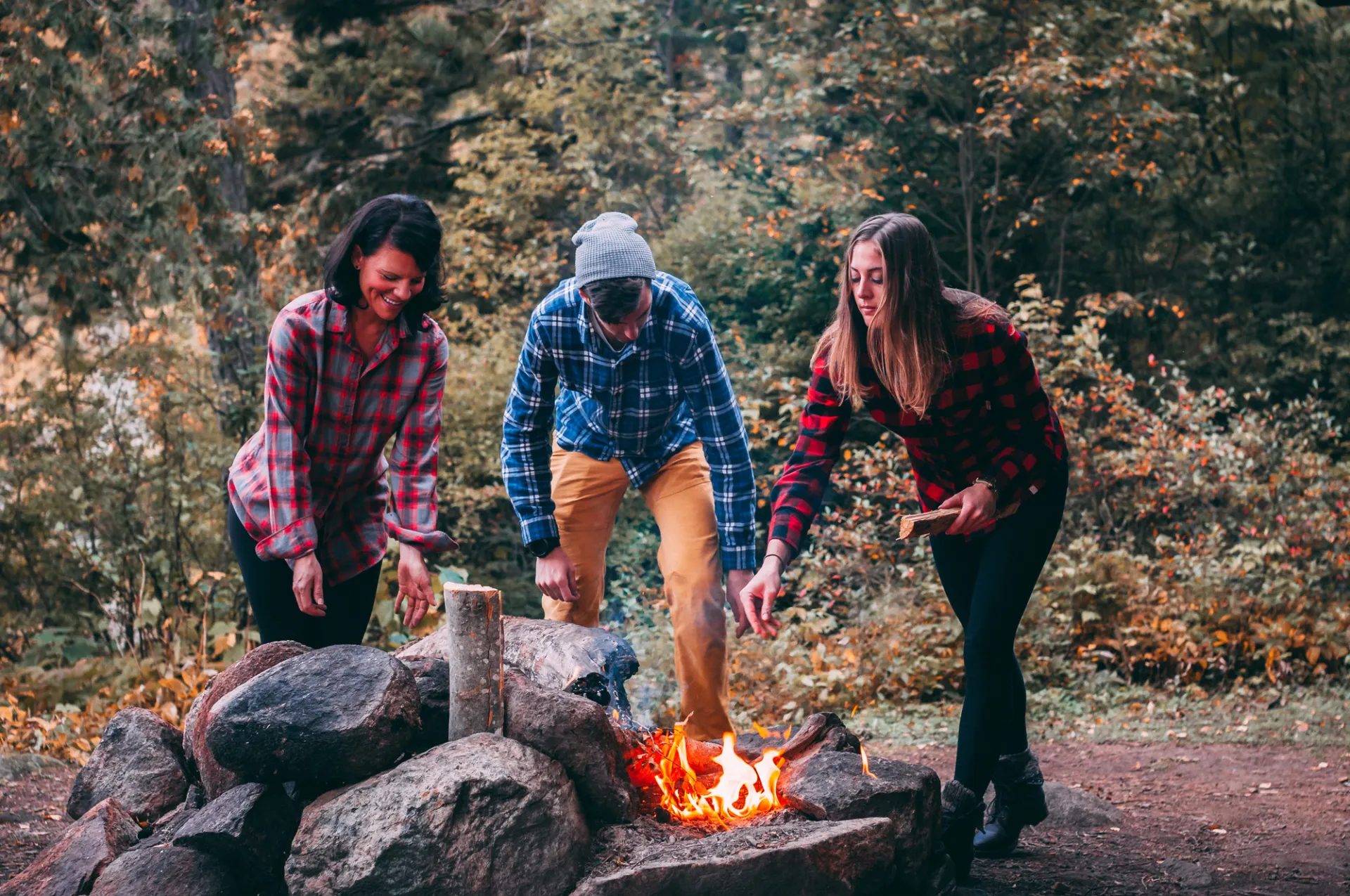 Three people tend to a fire. 