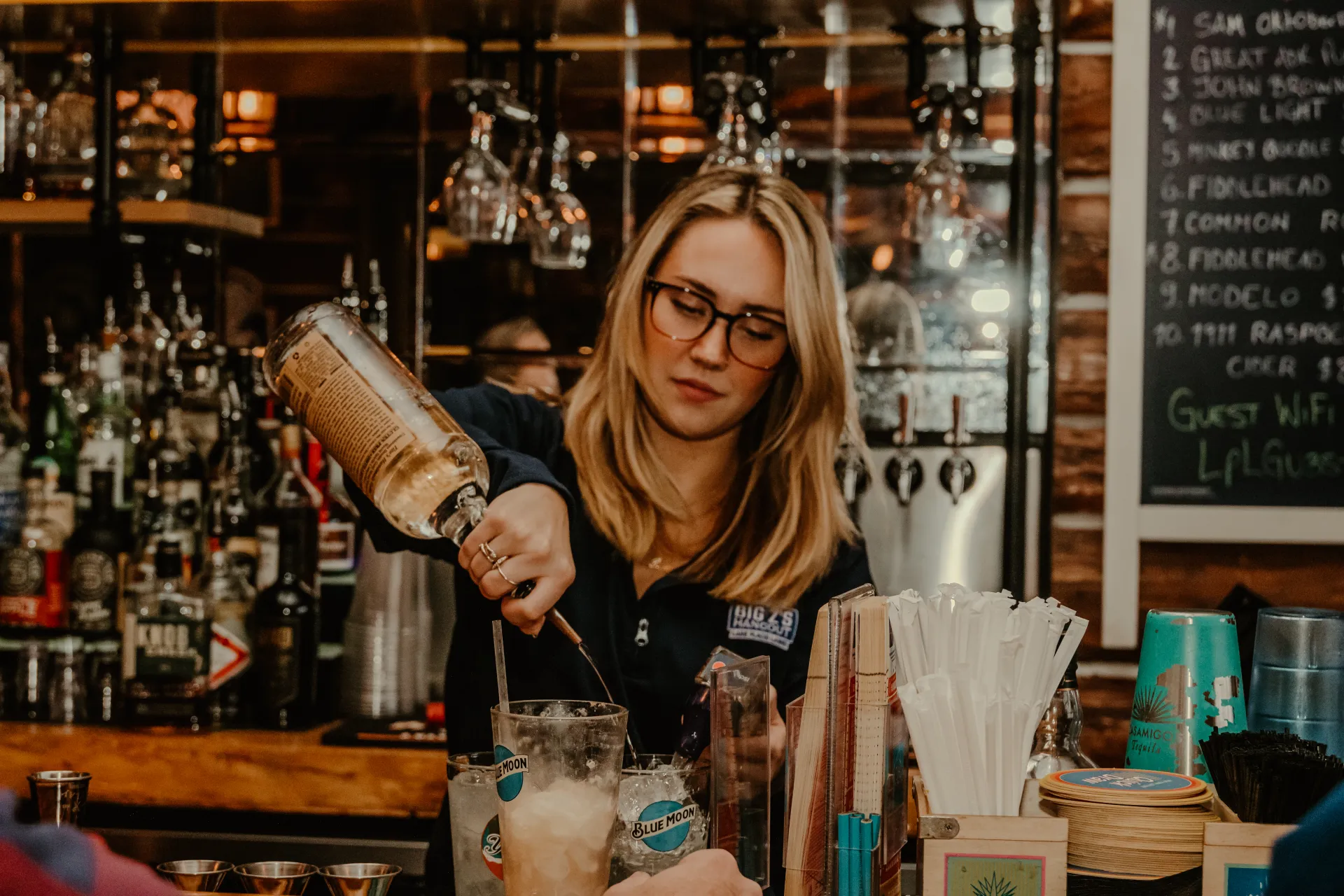 A smiling bar tender makes a cocktail with the full bar at Big Zs.  Photo Credit to A. Kelly.