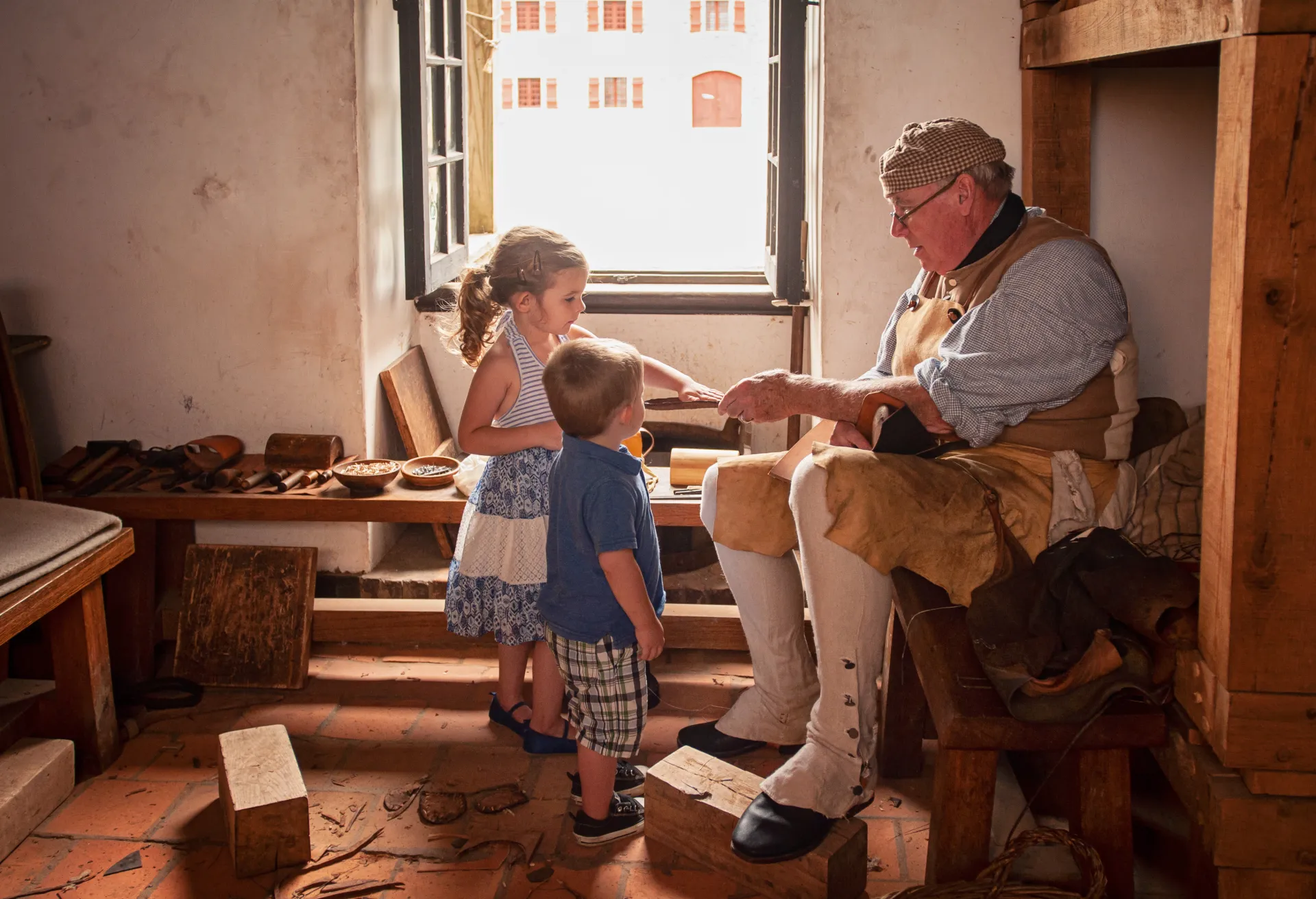 A young girl and boy feel the leather that a reenactment performer is crafting.